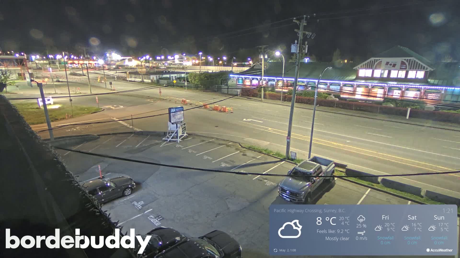A mostly clear night scene shows a highway intersection with several vehicles parked in a lot, and a building with lights along the roadside.