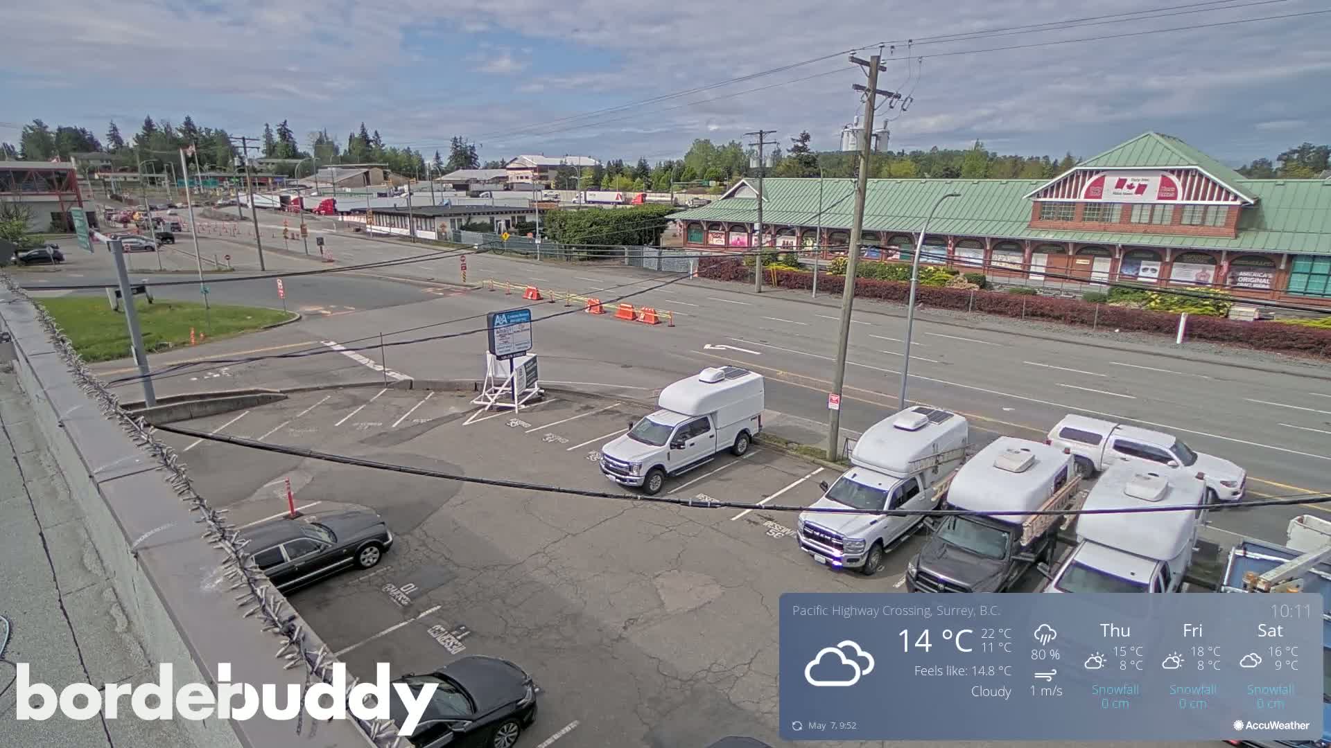 A cloudy day reveals a parking lot with several white trucks and cars, situated near a road and a large building.