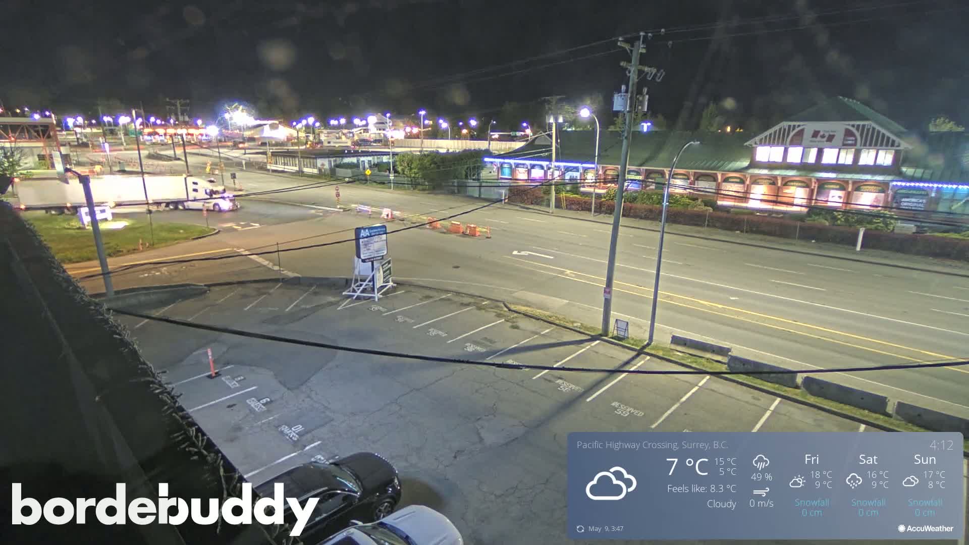 A nighttime, cloudy view of a highway crossing with a large parking lot, a few cars, and a semi-truck.