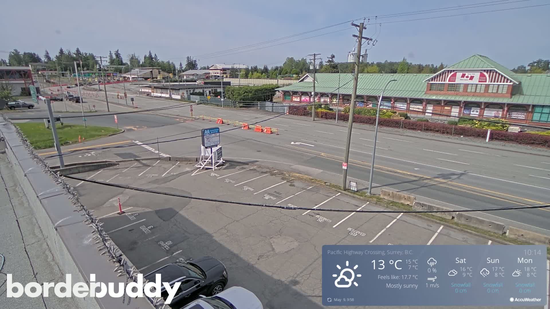 A mostly sunny, high-angle view shows a parking lot and roadway with a large building in the background.