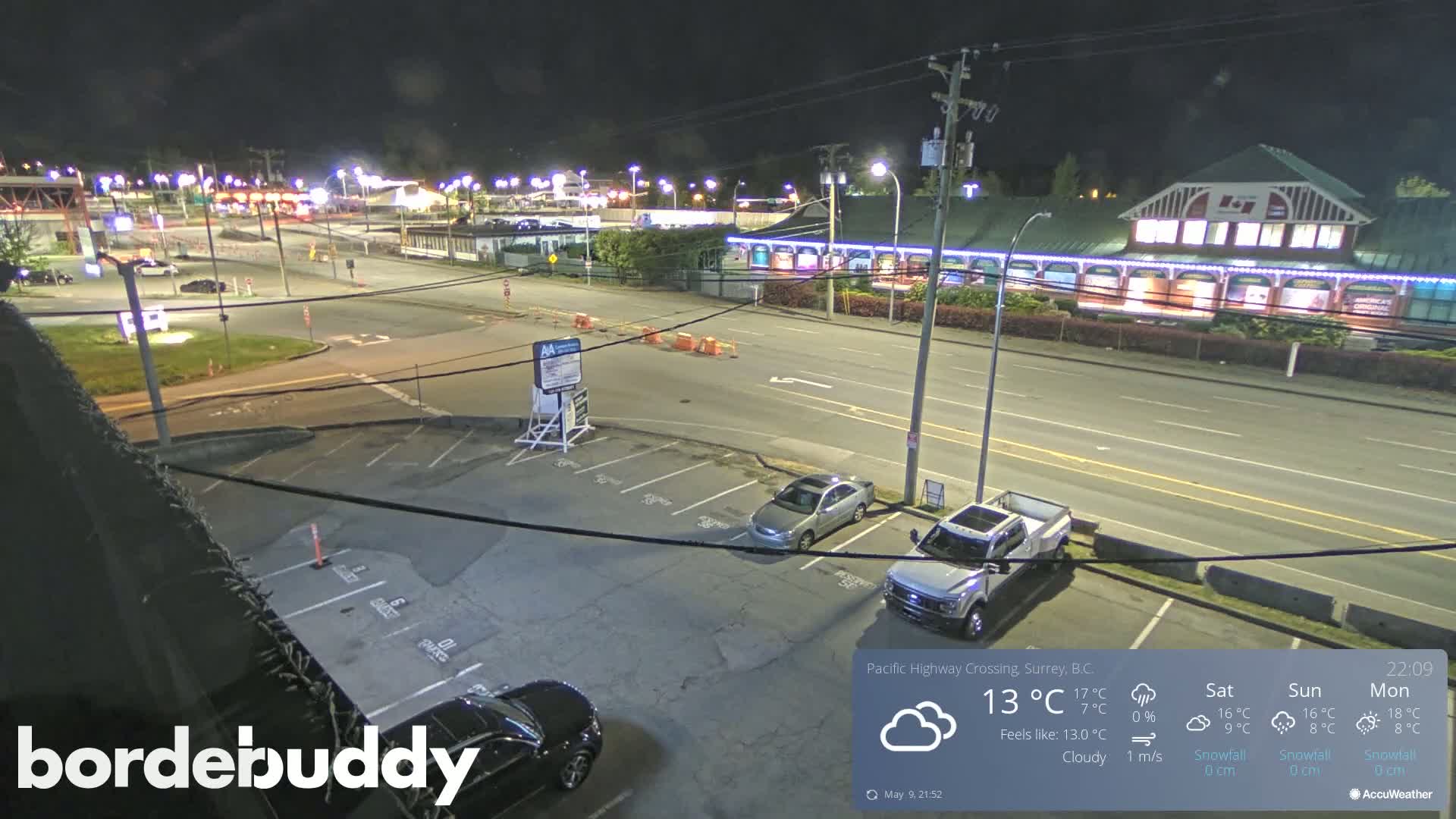 A nighttime, cloudy scene shows a parking lot with several cars and a street with buildings and traffic.