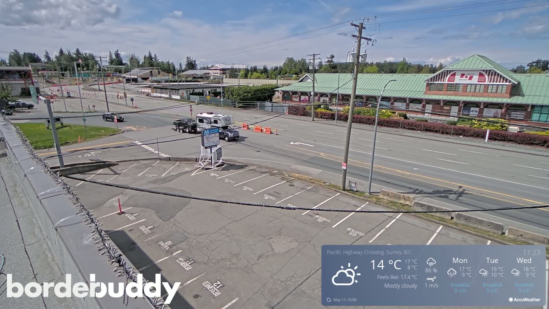 A mostly cloudy day reveals a high-angle view of a parking lot and roadway adjacent to a building complex, with a few vehicles present.