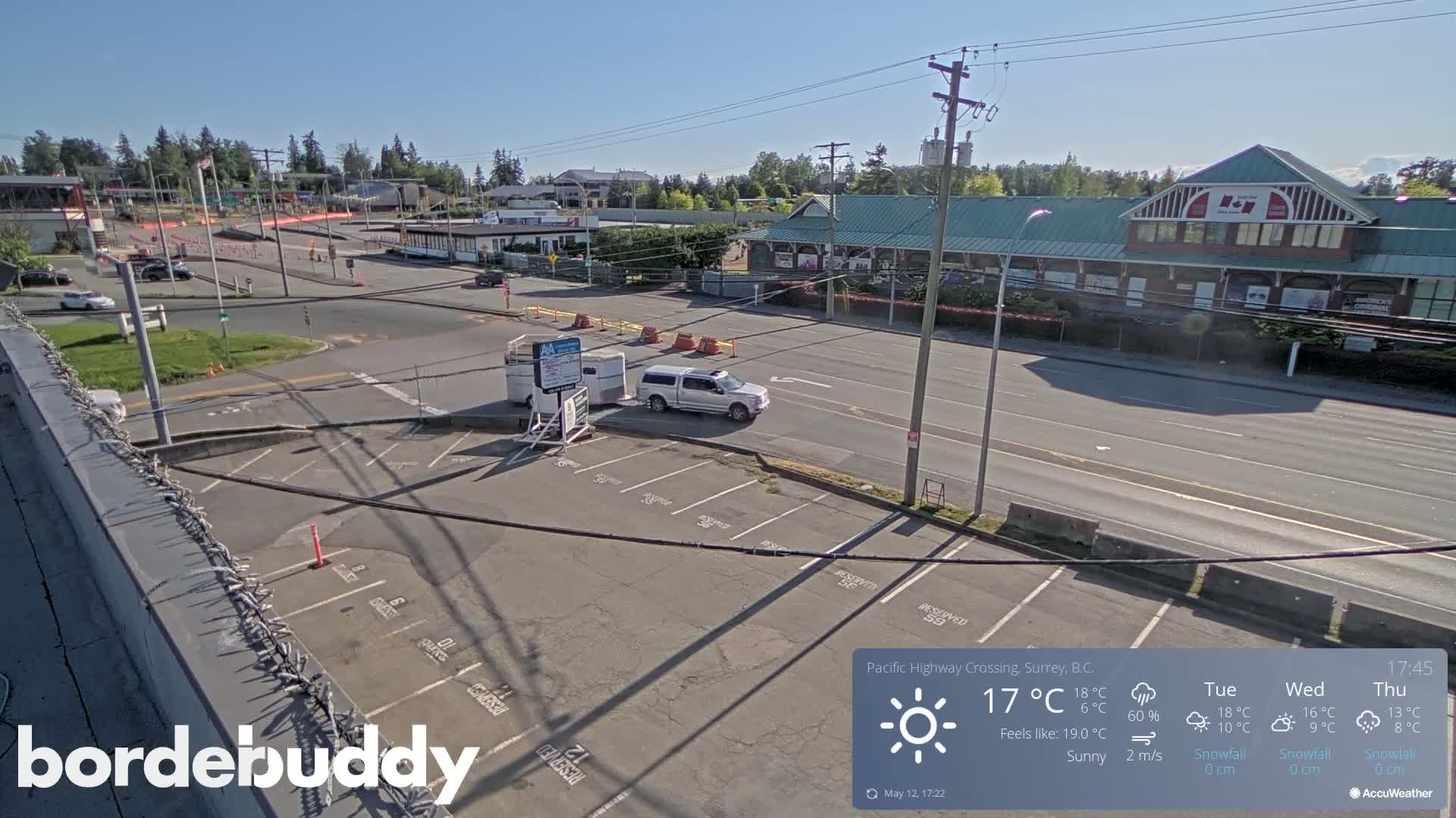 A sunny overhead view of a parking lot and roadway near a building complex, with a pickup truck parked in the lot.