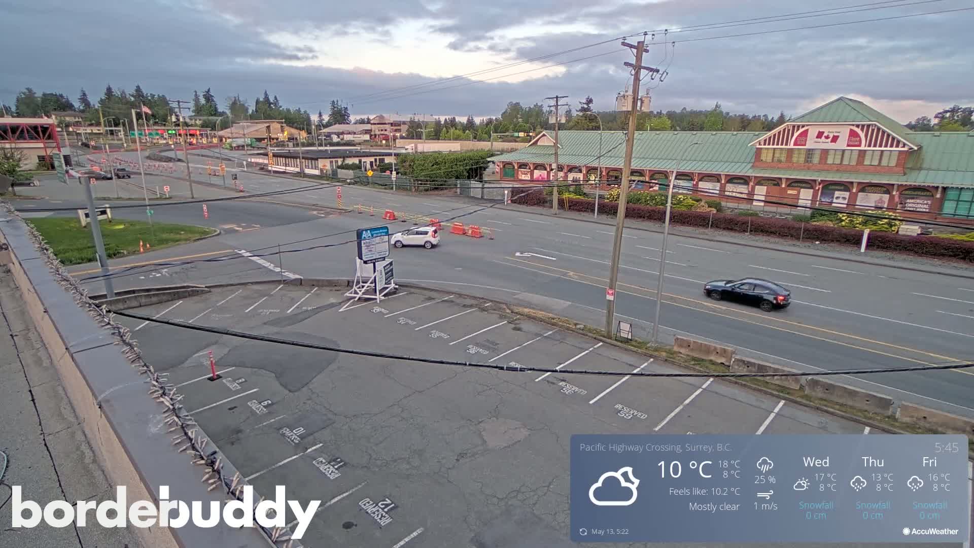 A mostly clear, overcast day reveals a parking lot and roadways leading to a commercial building, with a few vehicles visible.