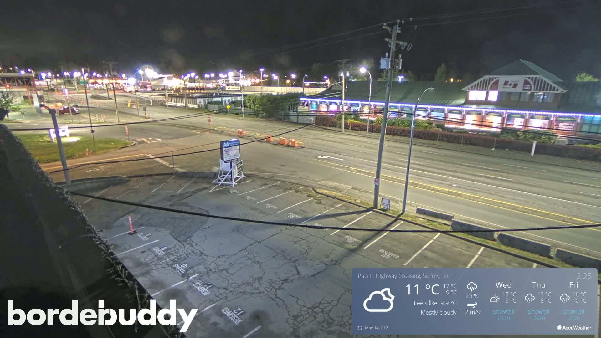 A mostly cloudy night scene shows a highway crossing with a parking lot and several buildings, some of which are illuminated.