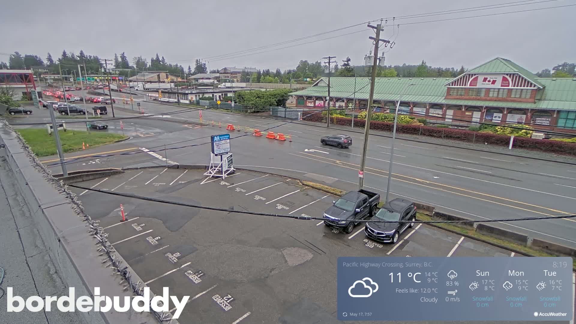 A wet, cloudy parking lot overlooks a roadway with sparse traffic under a gray sky.