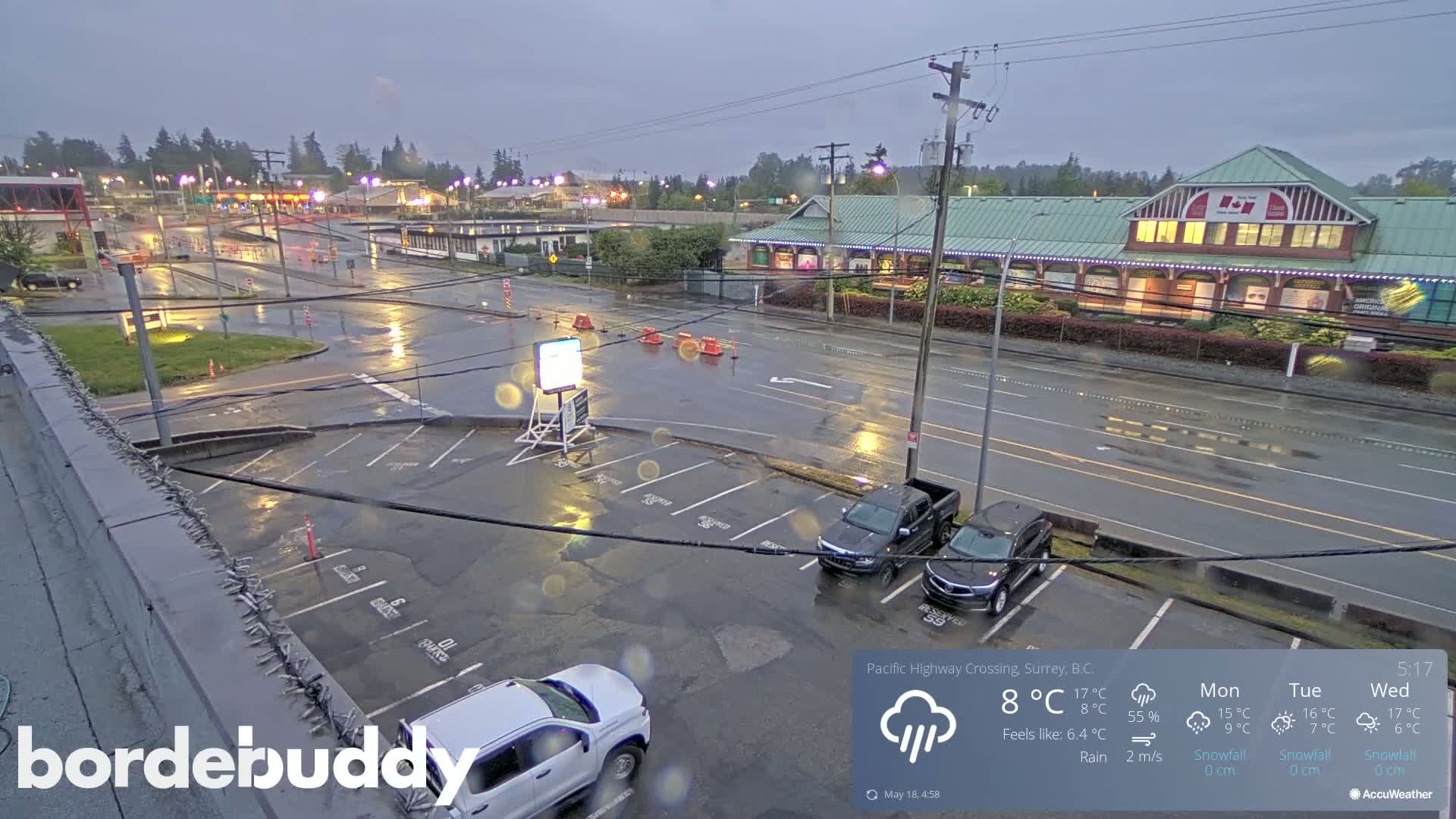 A wet parking lot and roadways are visible, under a rainy sky, with several vehicles parked and a building in the background.