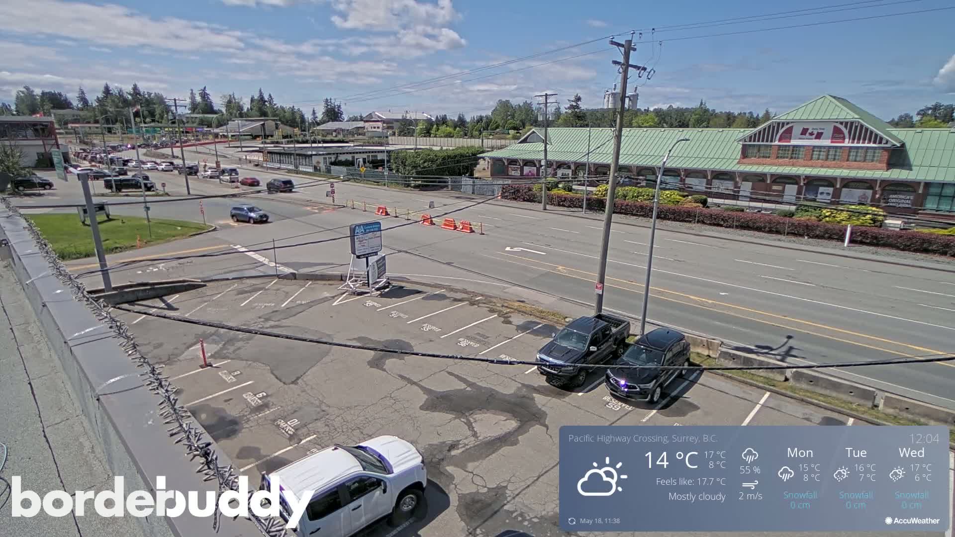 A mostly cloudy day reveals a parking lot, a roadway with several vehicles, and a long building with a green roof.