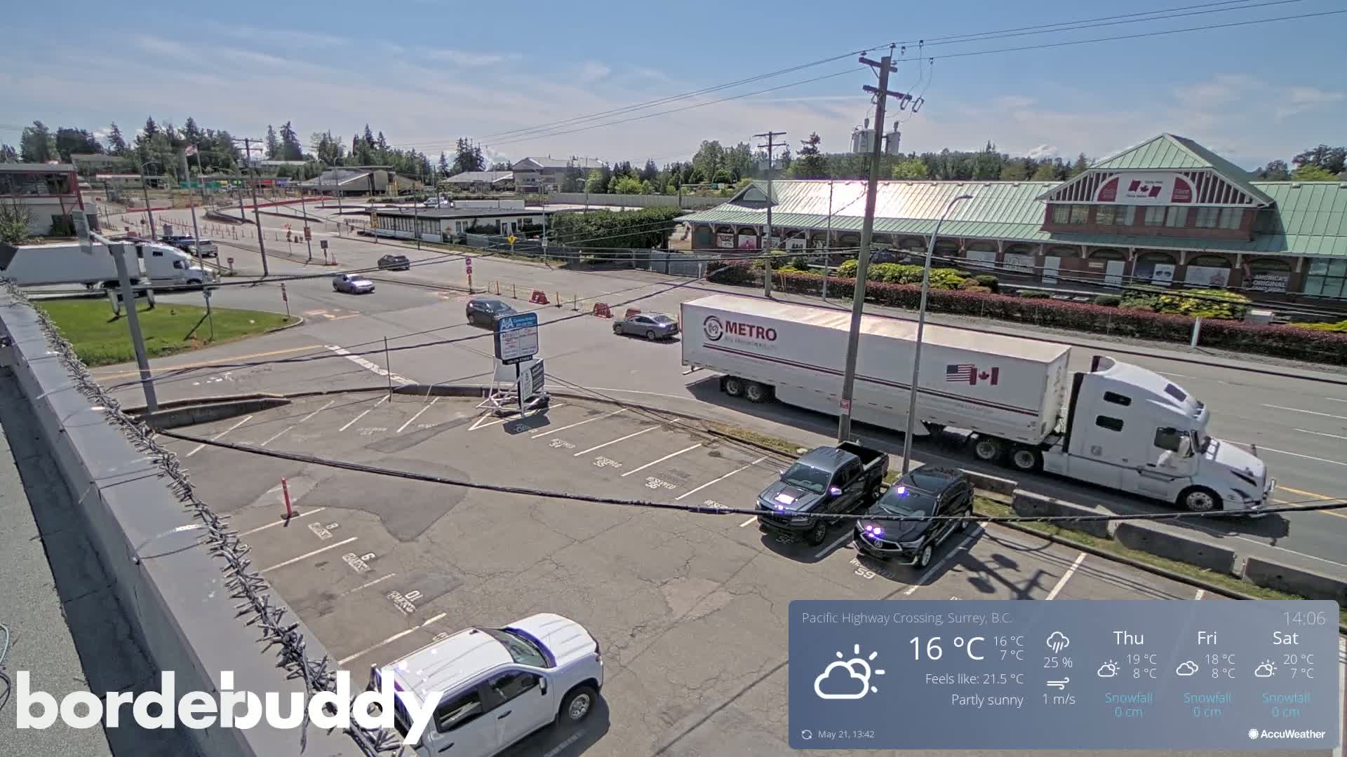 A partly sunny scene shows a highway intersection with several vehicles, including a large semi-truck, in a parking lot and on the road.