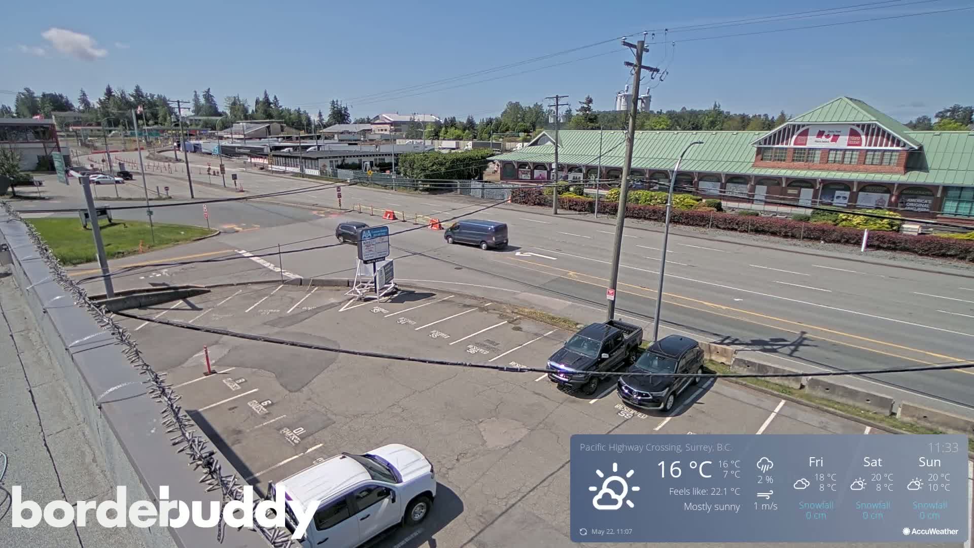 A mostly sunny parking lot with several vehicles and a street scene beyond, including a large building with a green roof.