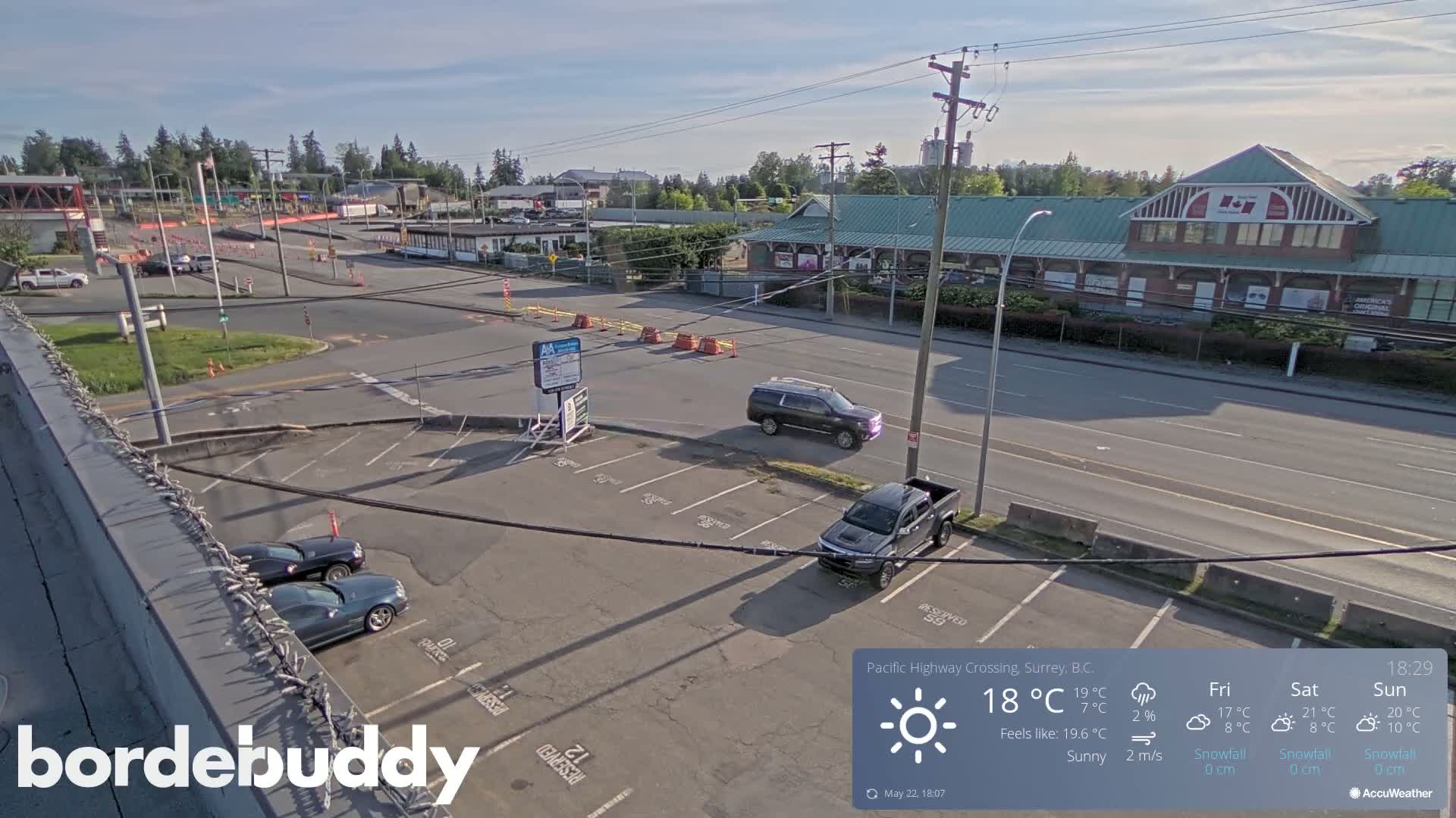 A sunny parking lot with several cars and a view of a street and buildings in the distance.