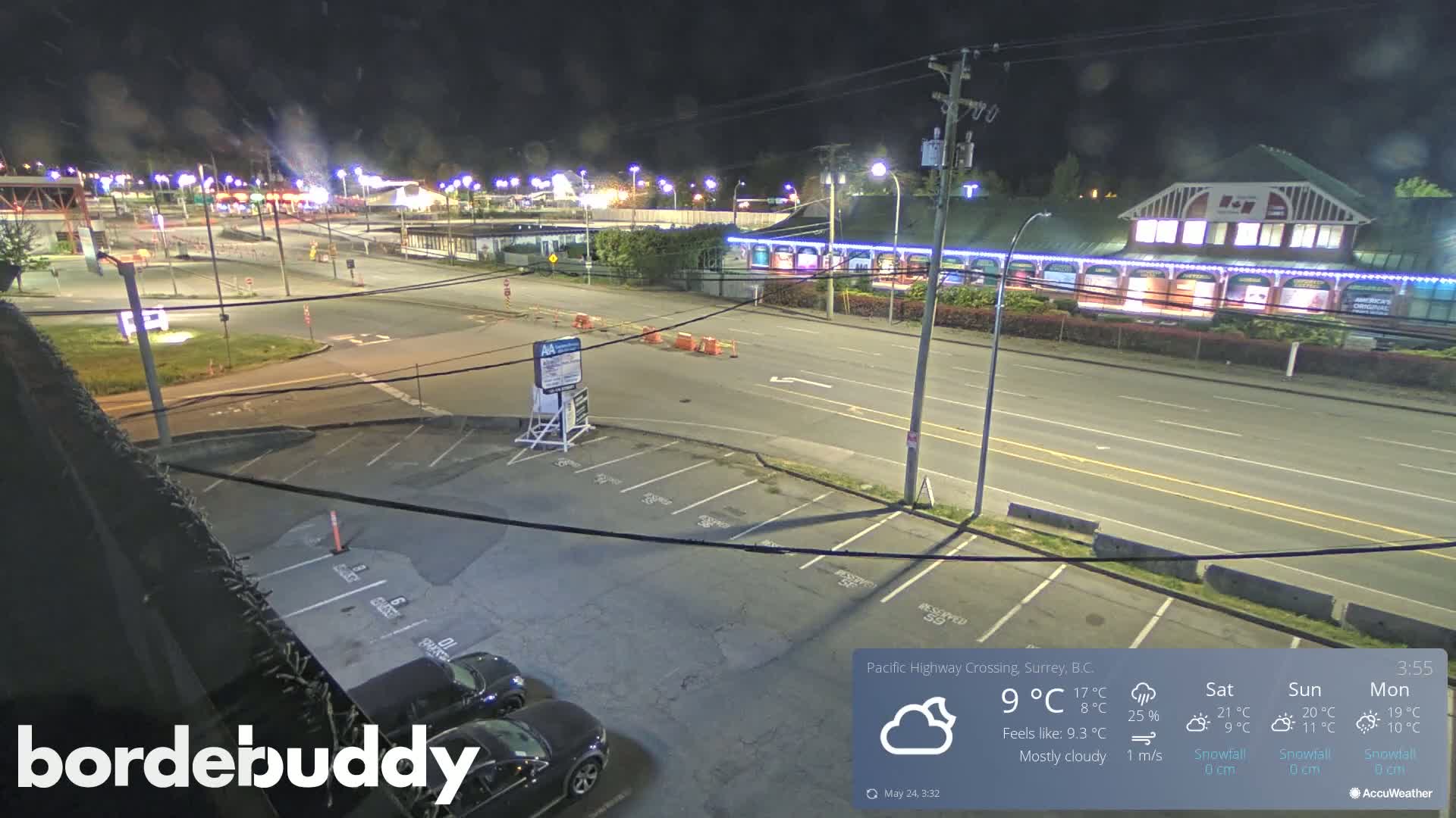 A mostly cloudy night scene shows a highway intersection with a parking lot and several buildings, some of which are illuminated.