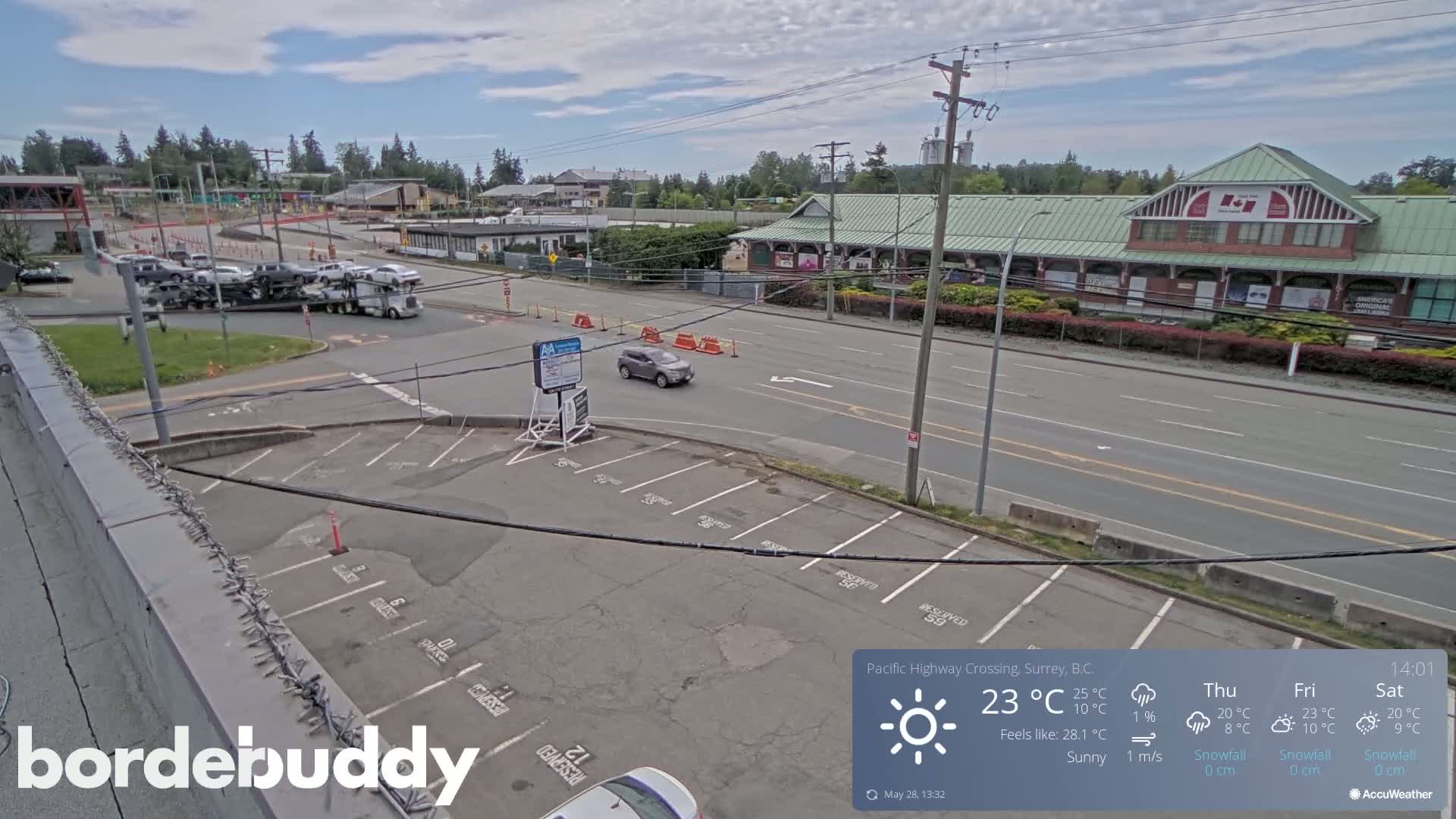 A sunny, street-level view of a parking lot and roadway next to a building, with a truck carrying multiple cars in the background.