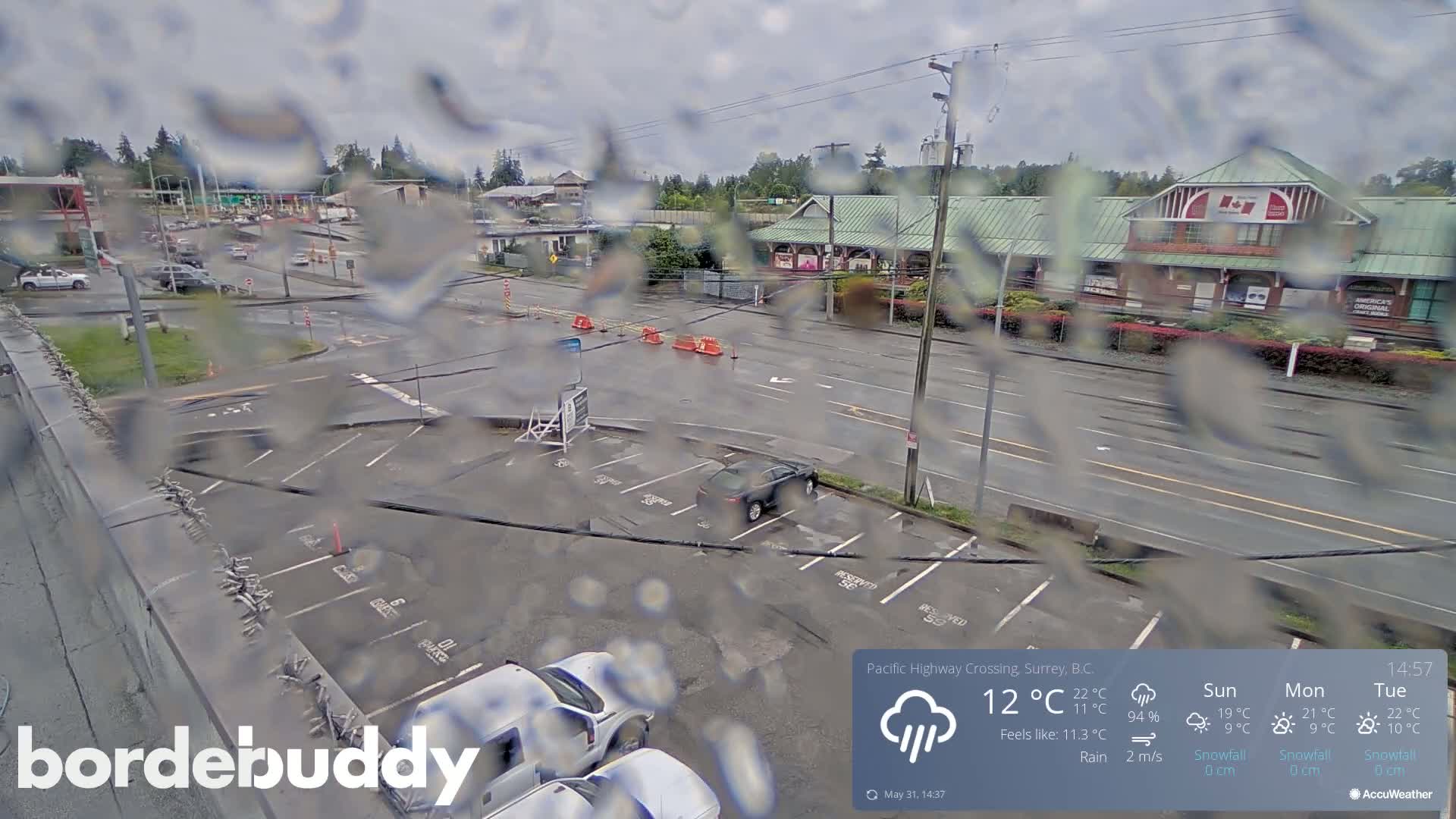 A rain-soaked view of a parking lot and roadway near a building, with several cars visible.
