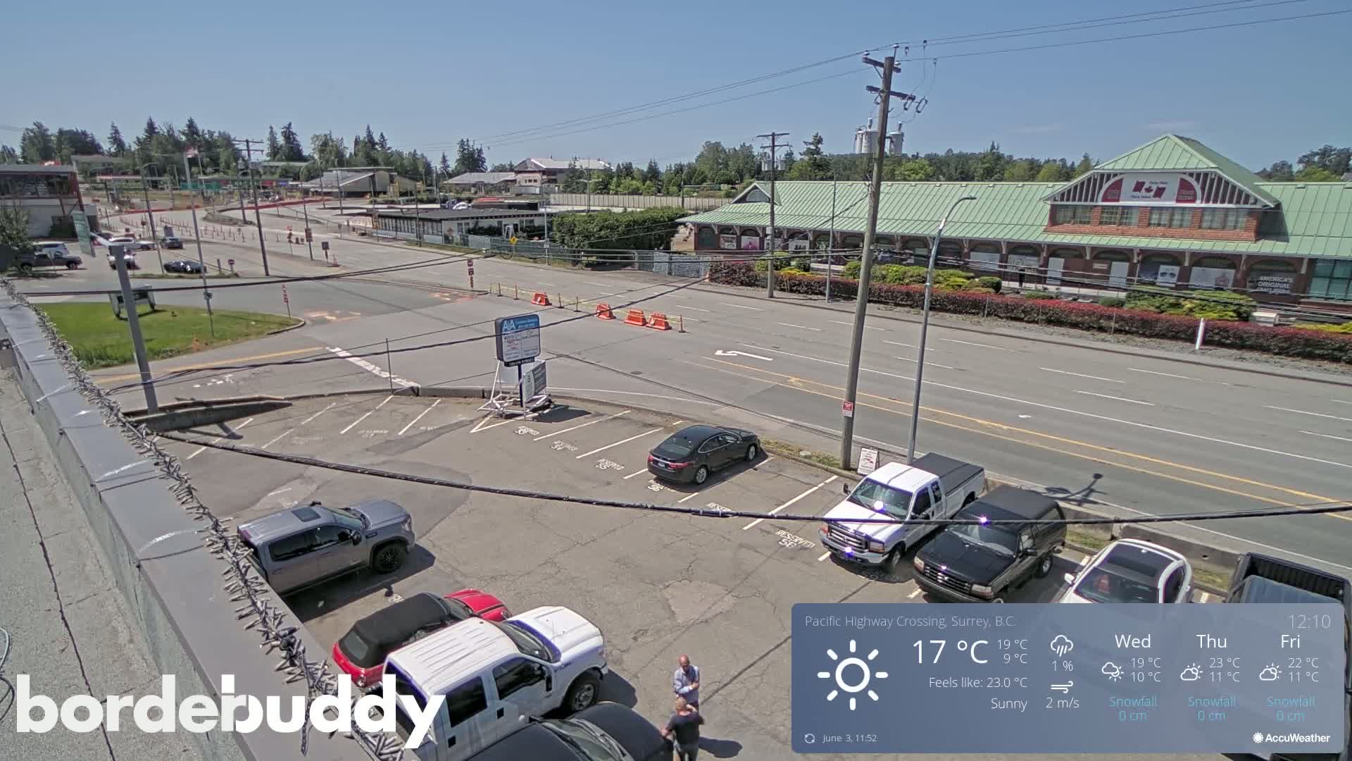 A sunny day reveals a parking lot and roadway with several vehicles, near a long building with a green roof.