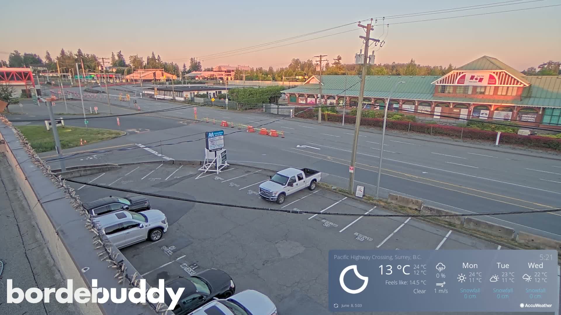 A mostly empty parking lot and roadway are visible under a clear sky at dusk, with several vehicles parked.