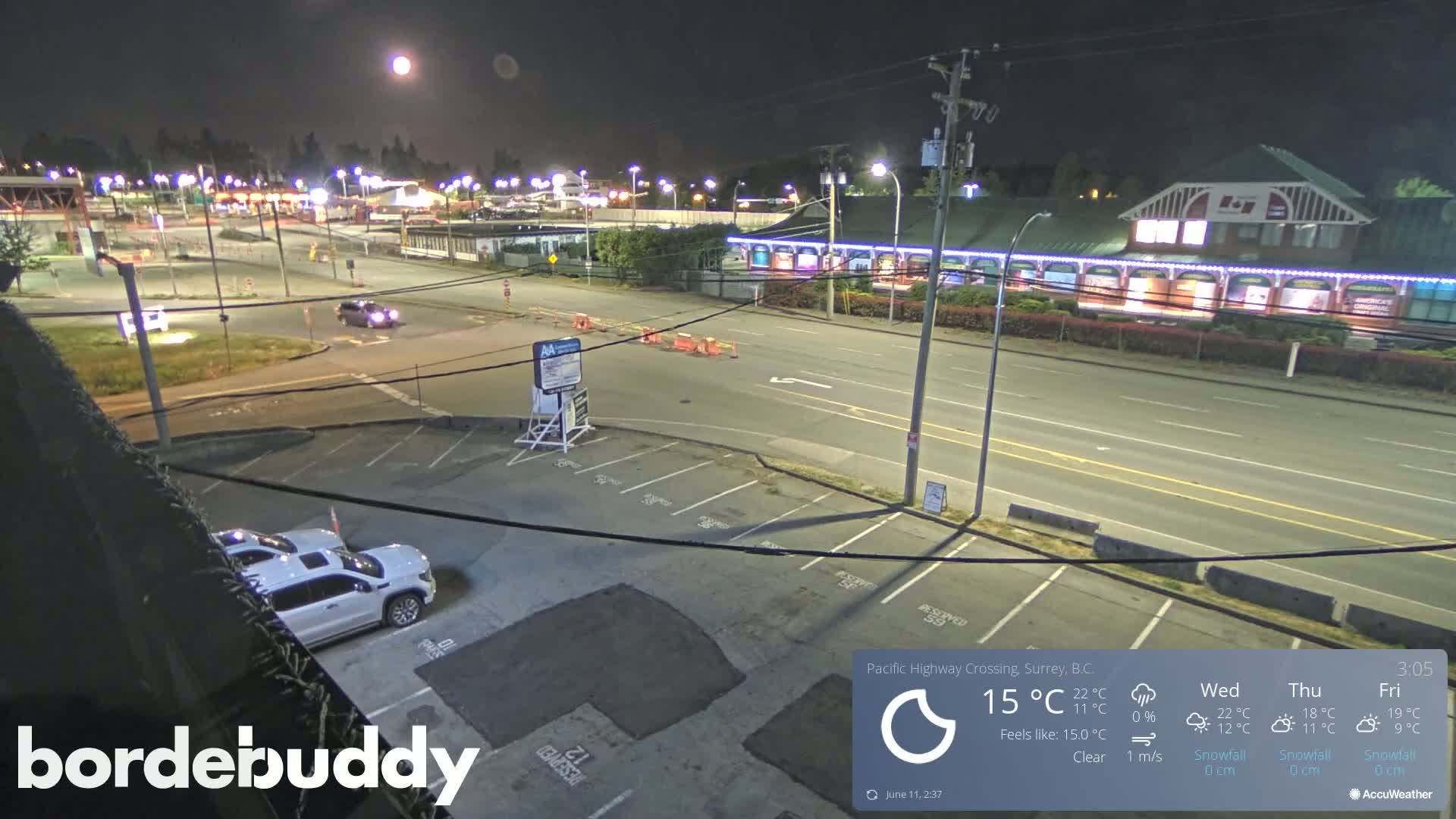 A nighttime overhead view of a highway crossing with a few cars in a parking lot and a building with lights under a bright full moon and clear skies.