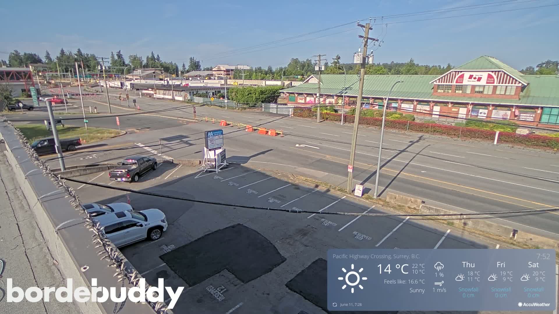 A sunny, overhead view of a parking lot and roadway near several buildings, some of which appear to be commercial.