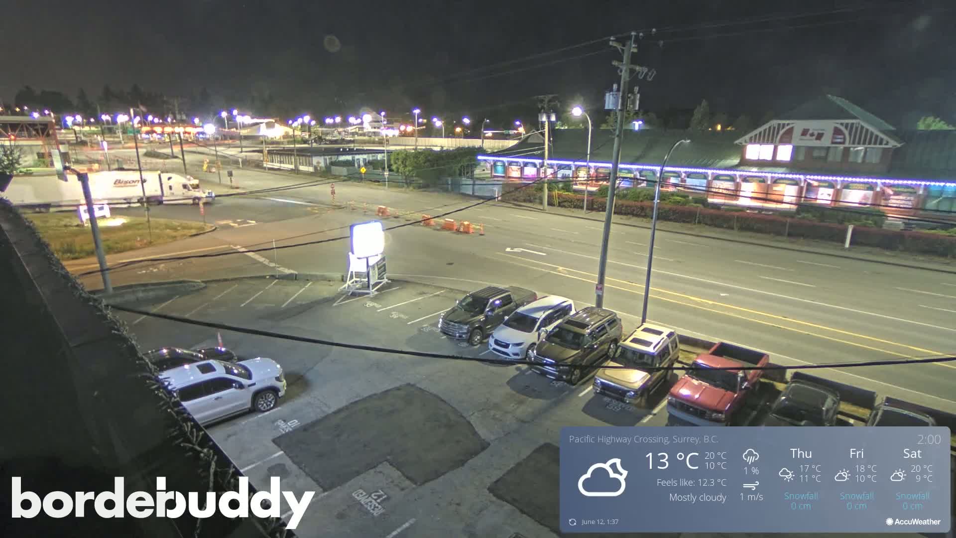 A mostly cloudy night scene shows a highway with several cars parked in a lot and a large truck stopped at an intersection.