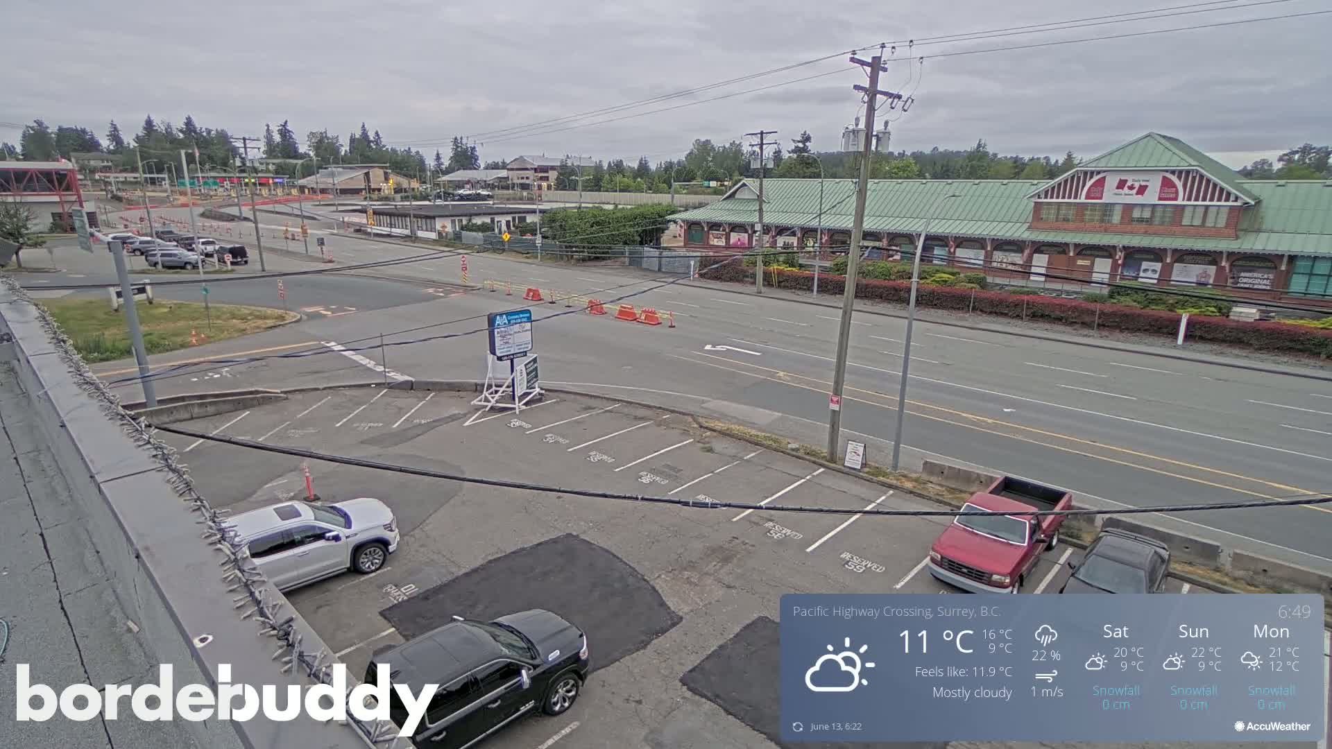 A mostly cloudy day reveals a parking lot, road, and buildings, including a large commercial structure, with several vehicles parked.