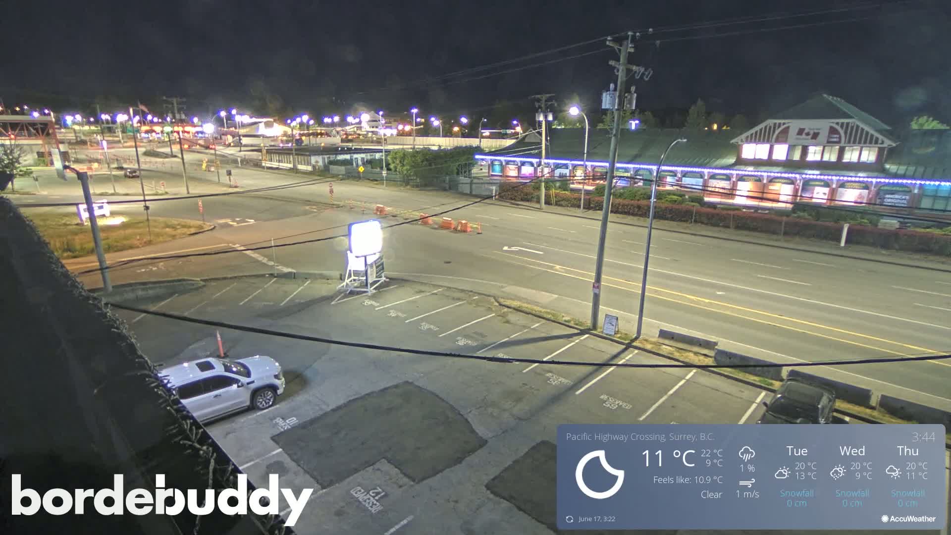 A nighttime, clear view of a highway crossing with a mostly empty parking lot, a few vehicles, and some buildings along the road.