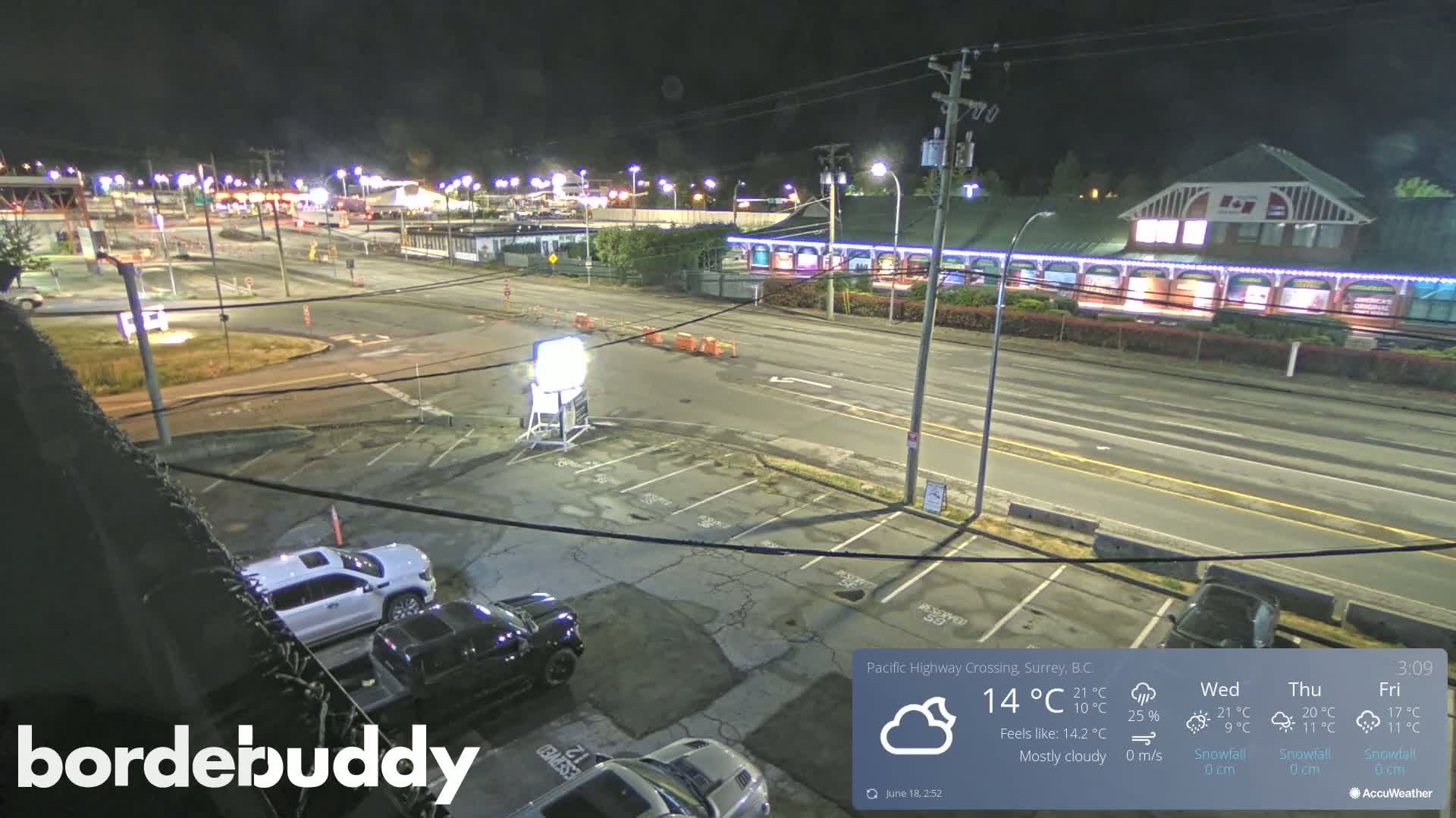 A mostly cloudy night scene shows a highway intersection and parking lot with several vehicles, under bright streetlights.