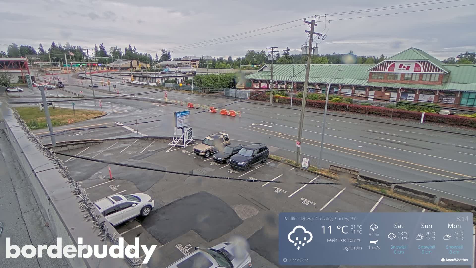 A wet parking lot and roadway with several vehicles are visible, under a lightly raining sky, near a building and intersection.