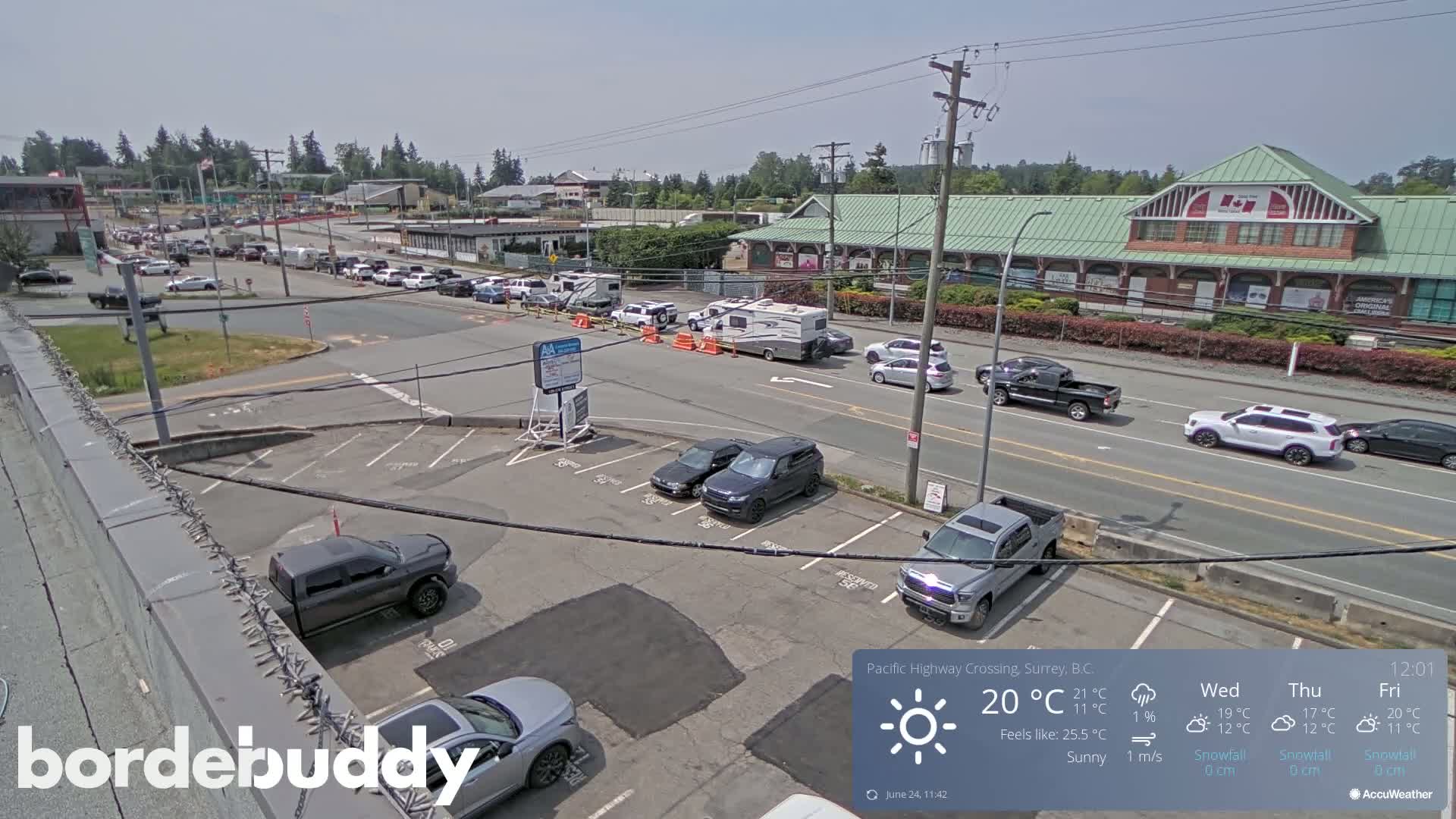 A sunny day reveals a parking lot and roadway with numerous vehicles, including cars, trucks, and an RV, near a large building.