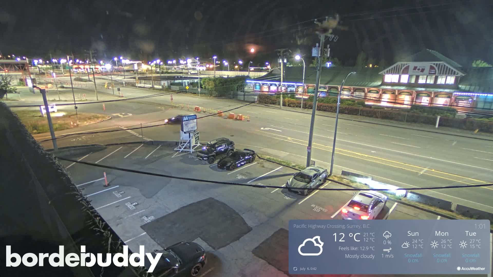 A nighttime view of a mostly empty parking lot and roadway near a building, under mostly cloudy skies.