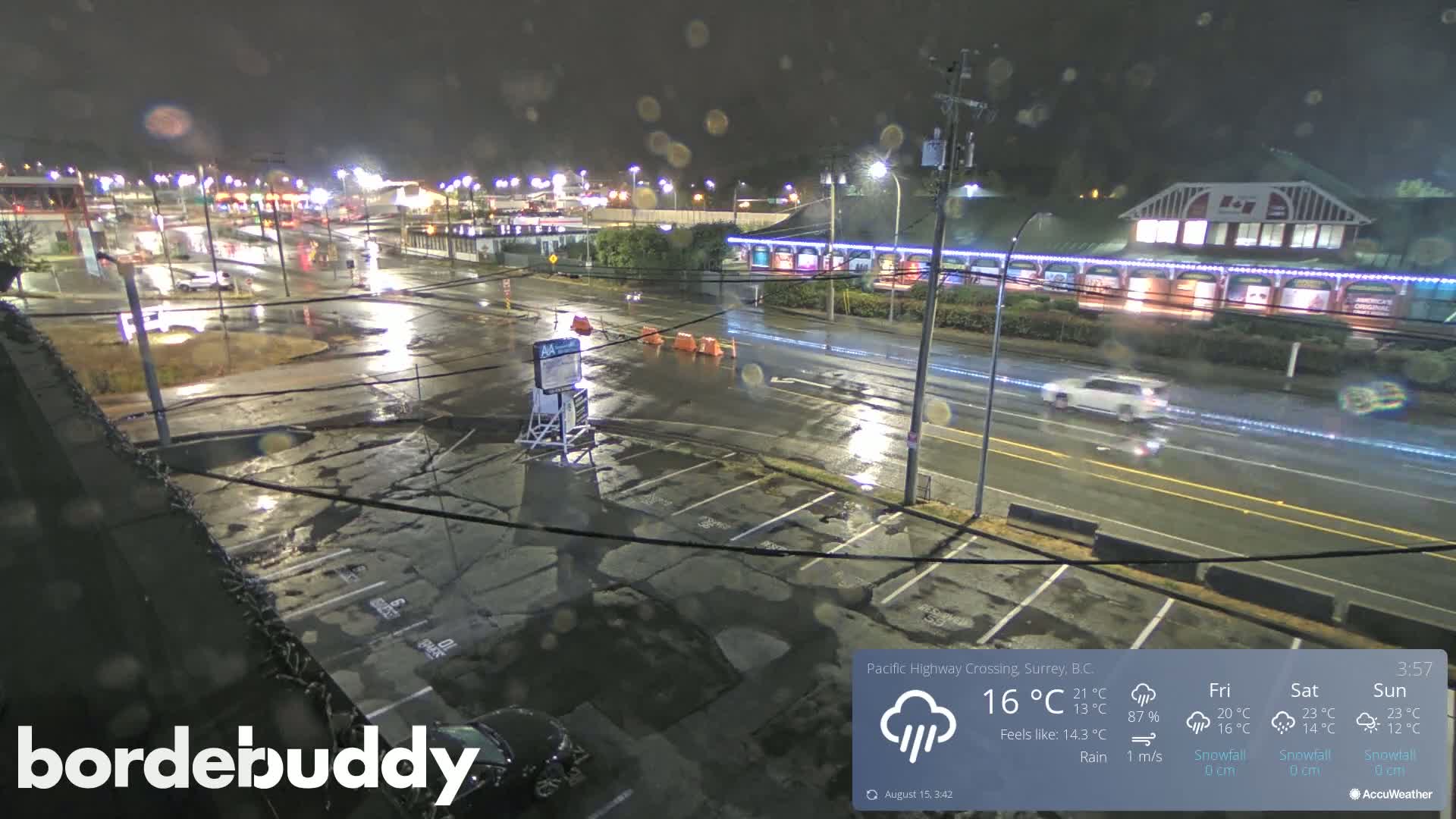 A nighttime view of a parking lot and roadway with several cars parked, under clear skies.