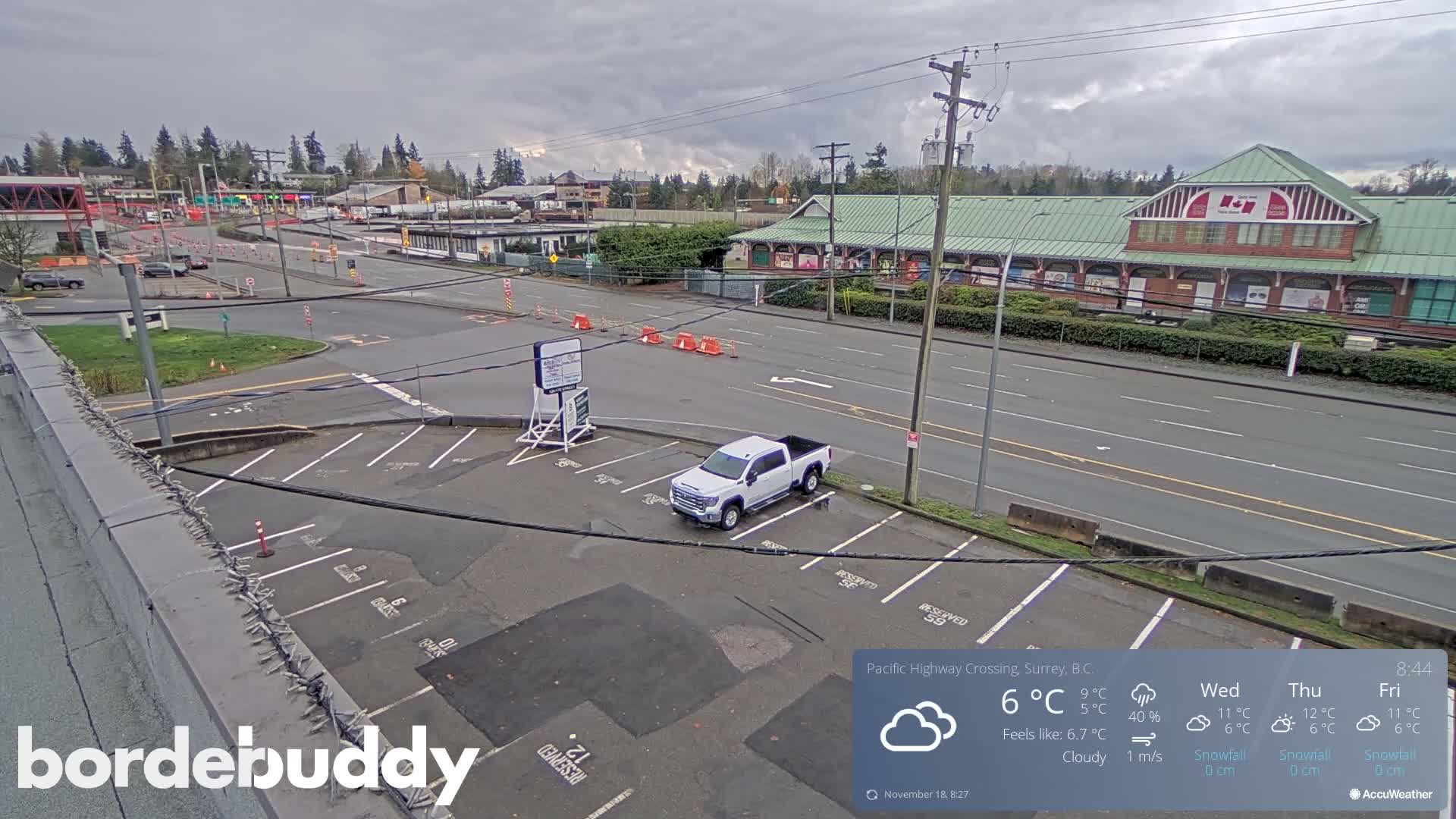 A nighttime view of a parking lot and roadway with several cars parked, under clear skies.