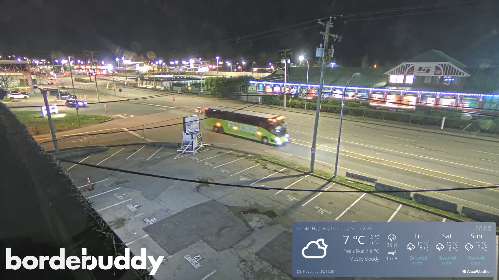 A nighttime view of a parking lot and roadway with several cars parked, under clear skies.