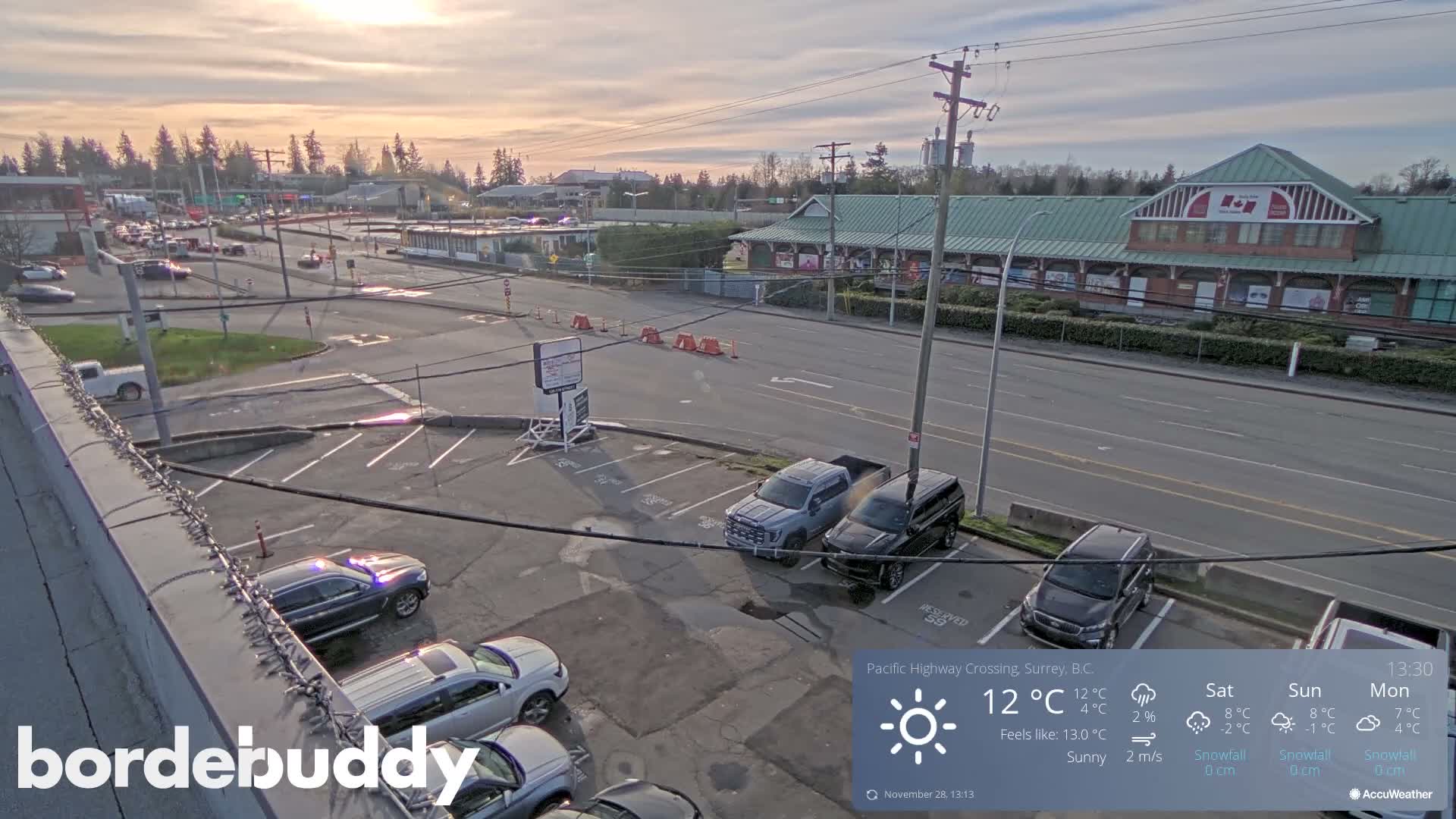 An elevated view shows a street with traffic, several parking lots with cars, and commercial buildings under a bright, partly cloudy sky.