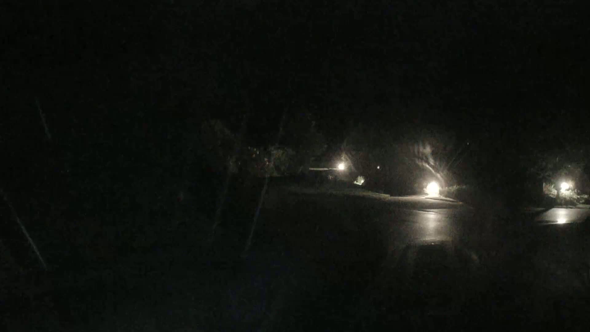 A dark, wet street at night is dimly lit by several streetlights.