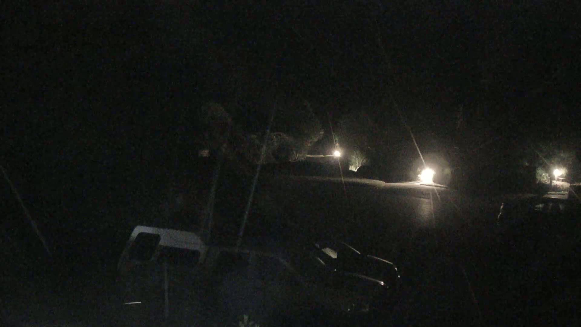 Several vehicles are parked in a dark, nighttime lot illuminated by sparsely placed lights.