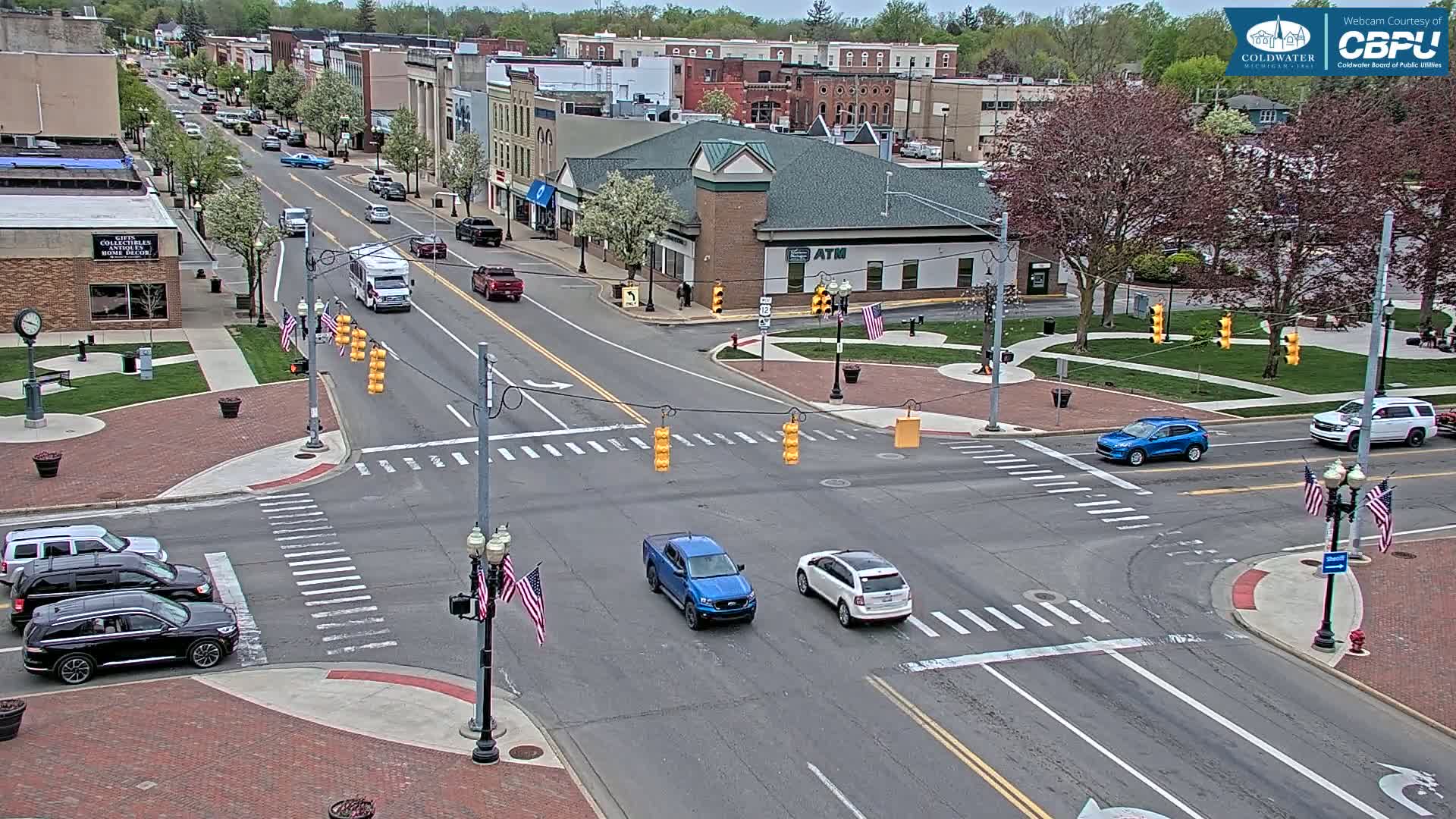 A street intersection in a town with several cars at a traffic light, under a partly cloudy sky.