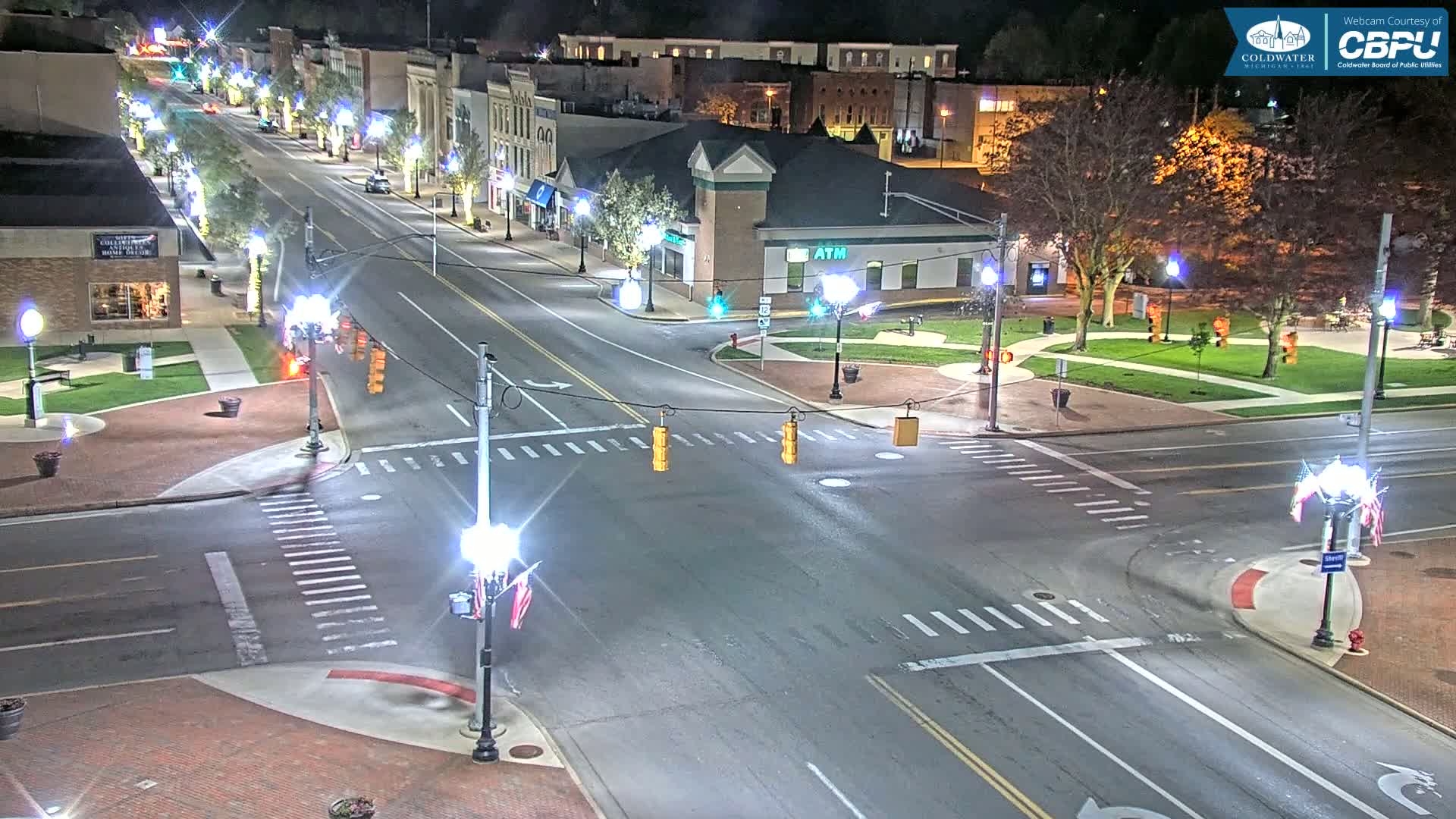 A nighttime, high-angle view of a town square intersection with a few cars, streetlights, and buildings lining the streets.