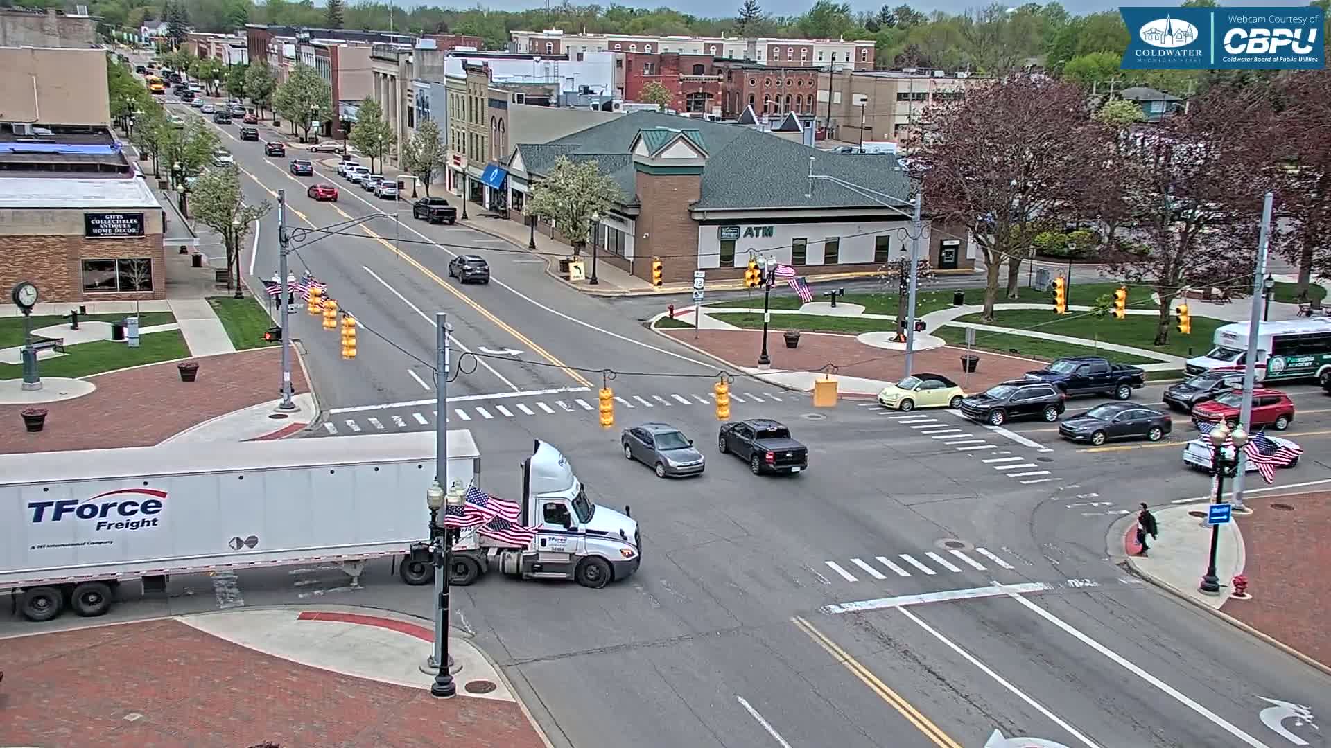 A semi-truck and several cars navigate a town square intersection on a partly sunny day.