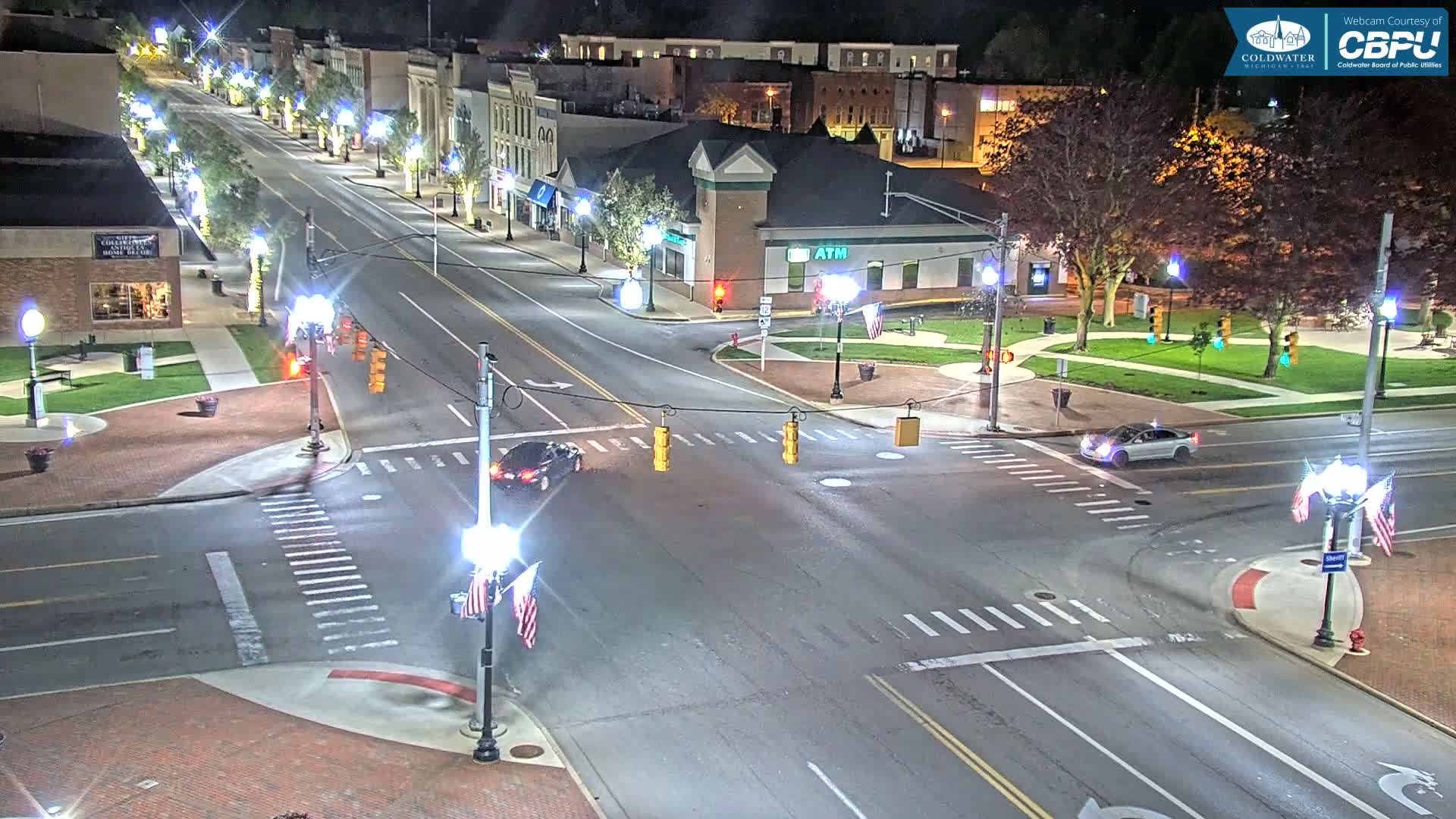 A nighttime aerial view of a town square intersection with cars and traffic lights, under clear skies.