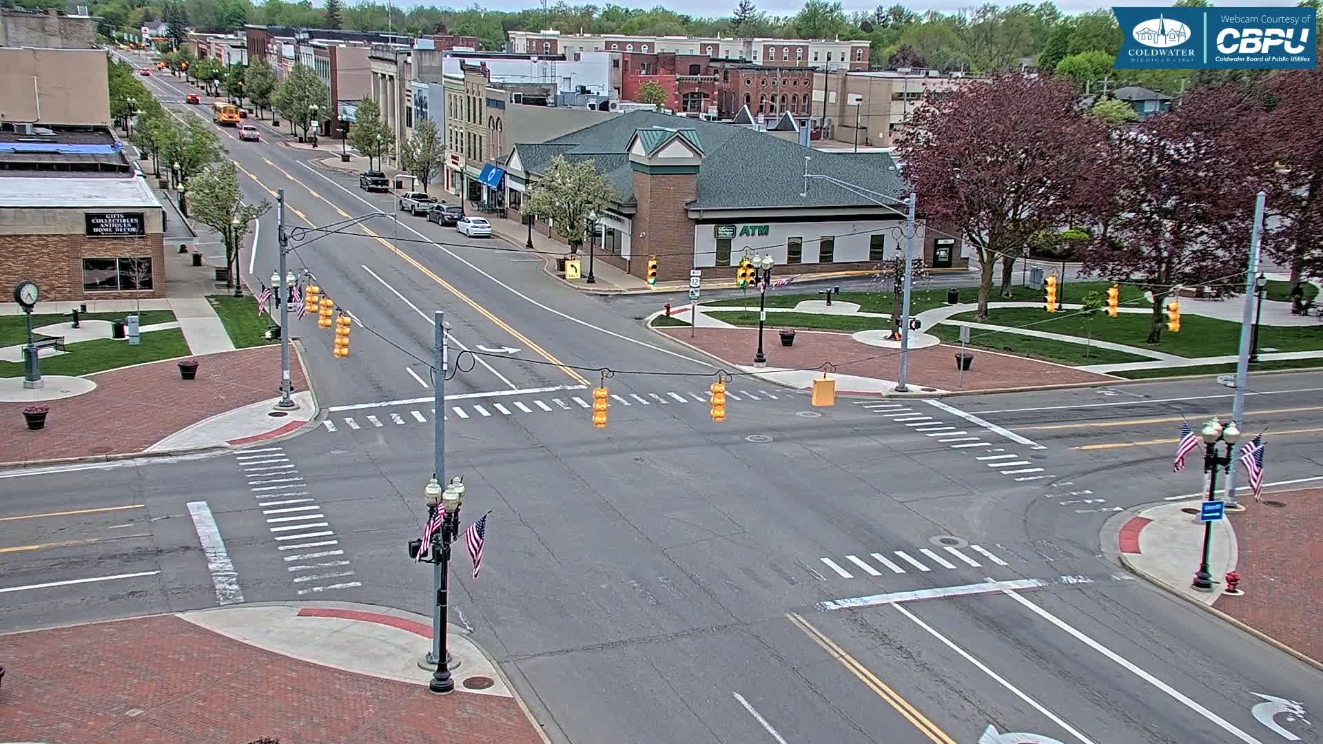 A mostly empty street intersection in a town on a partly cloudy day, with brick sidewalks and buildings lining the street.