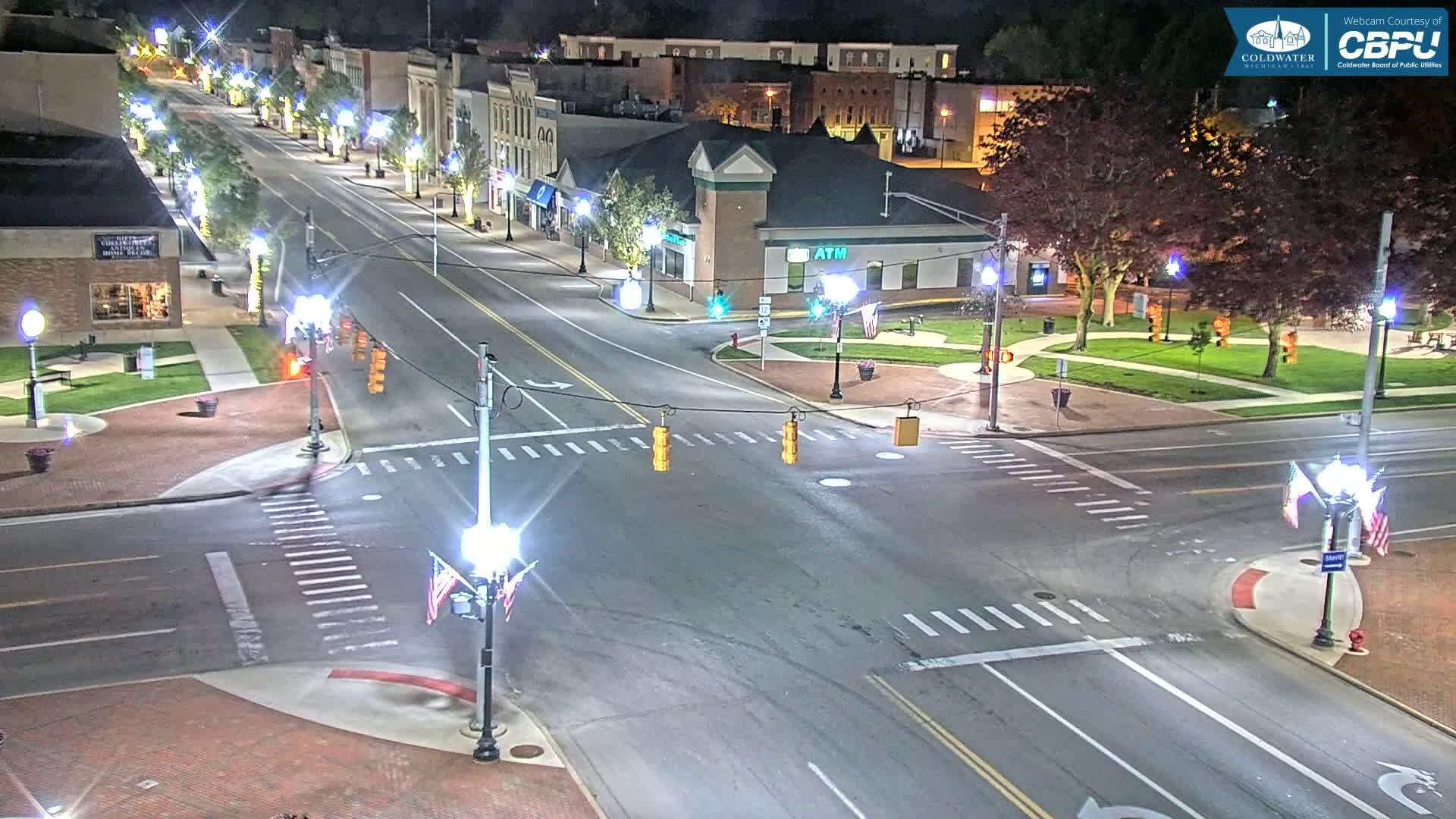 A nighttime view of a mostly empty town square intersection with several buildings, trees, and streetlights.