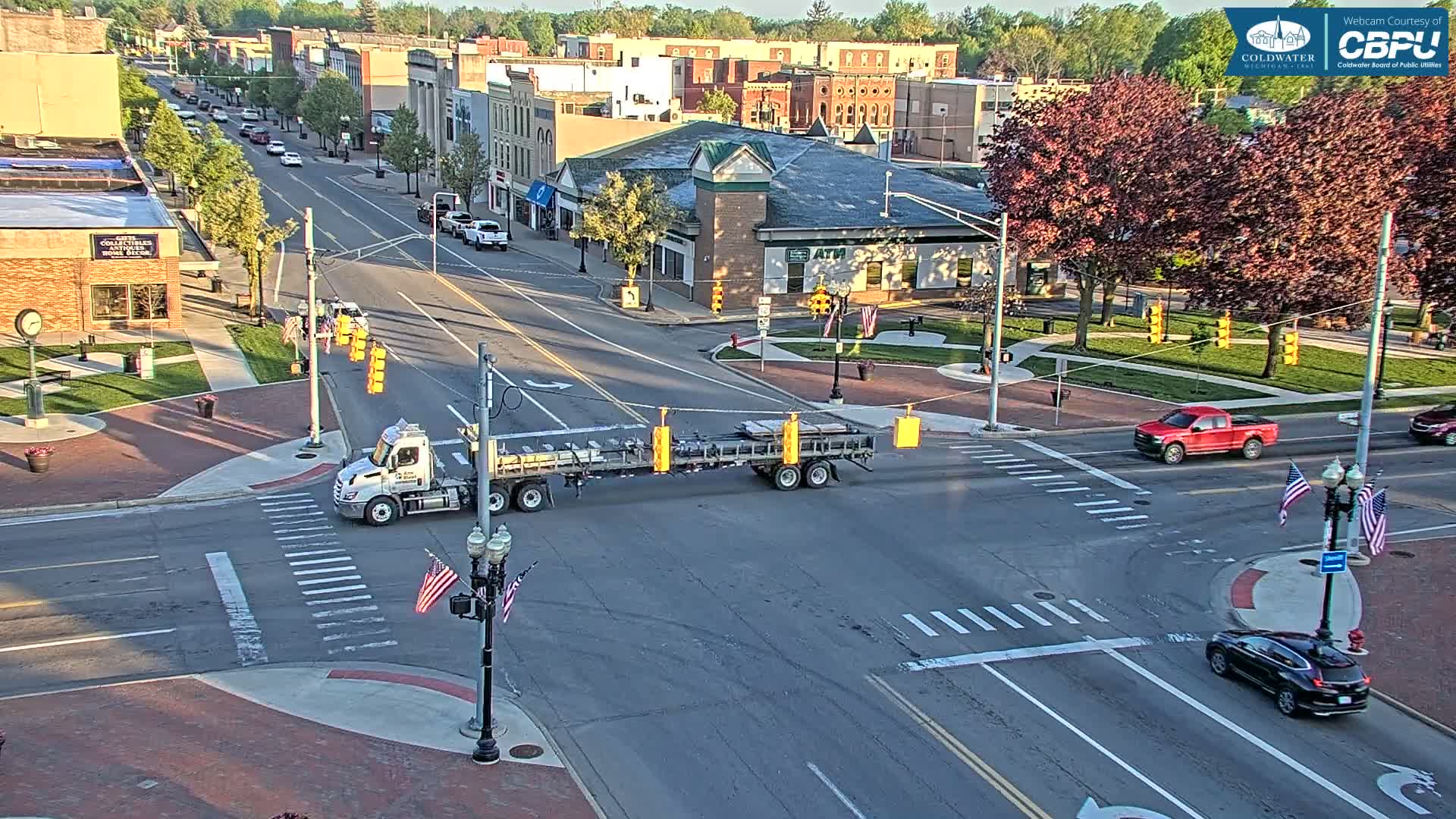A semi-truck is crossing a four-way intersection in a town on a partly sunny day.