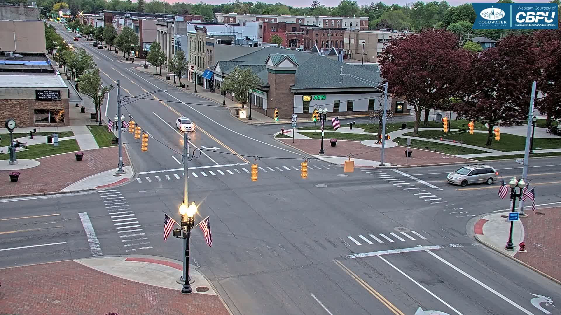An overhead view of a town square intersection shows several cars at a traffic light under a partly cloudy sky.