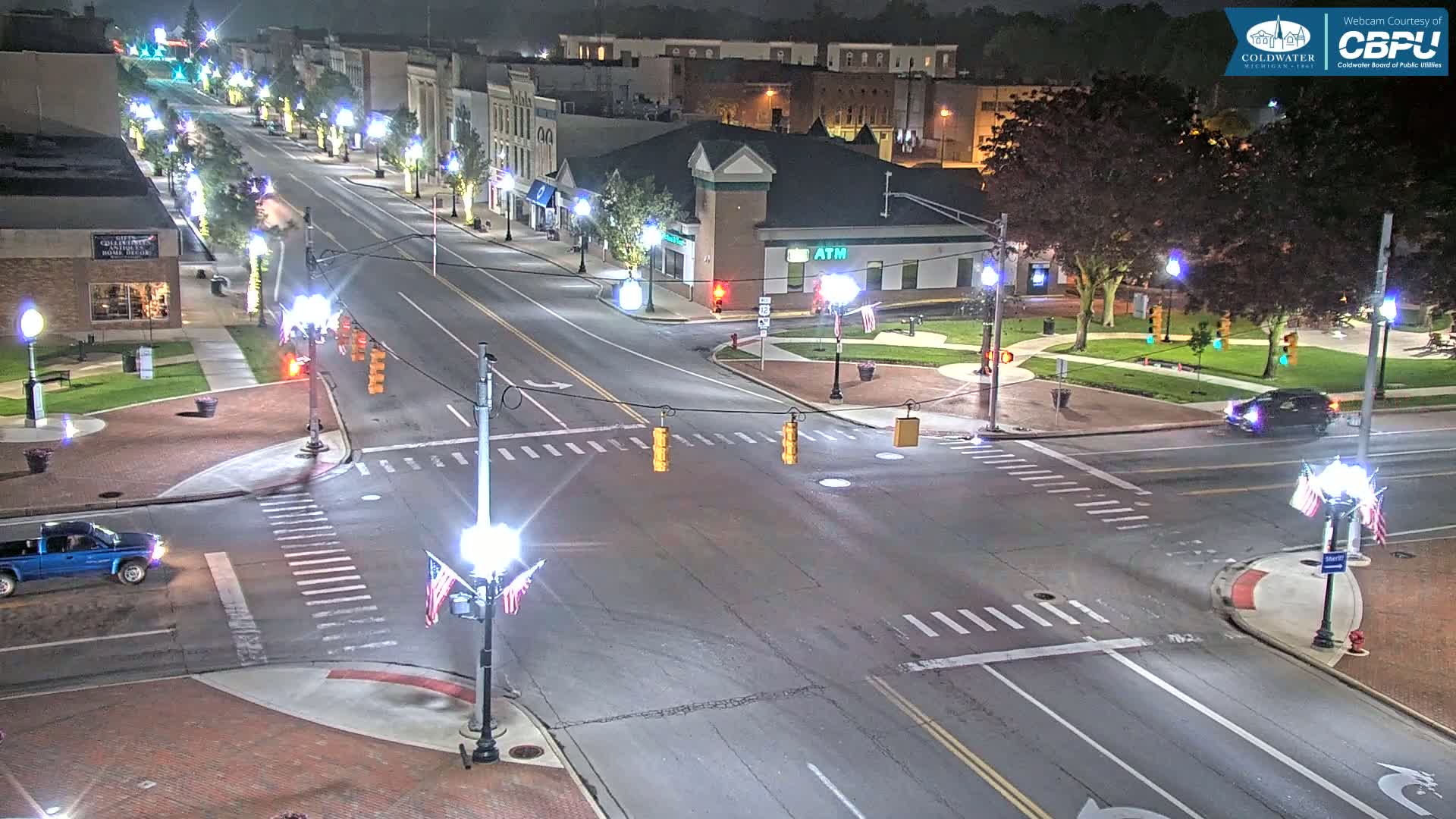 A nighttime view of a street intersection in a town, with a few cars and streetlights illuminating the scene.