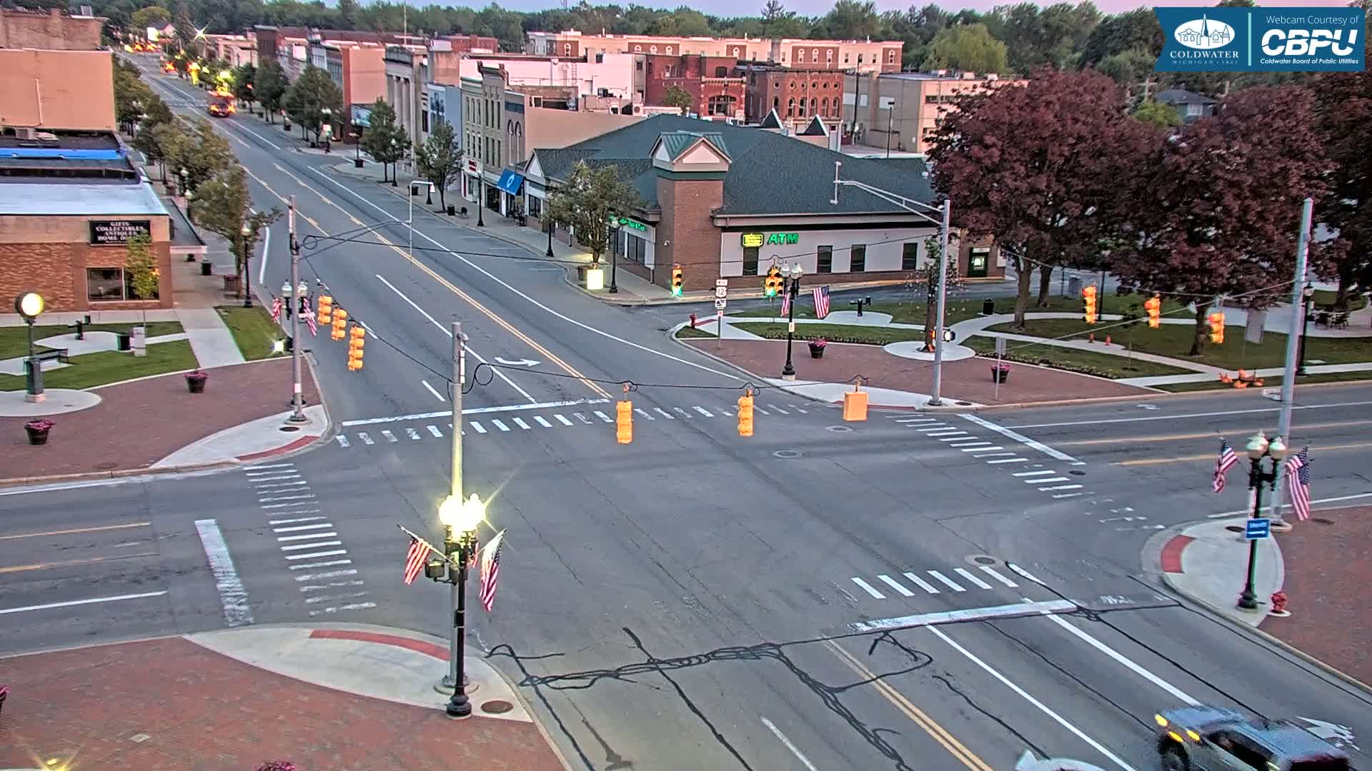 A high-angle, long shot of a four-way intersection in a town with buildings lining a street under a twilight sky.