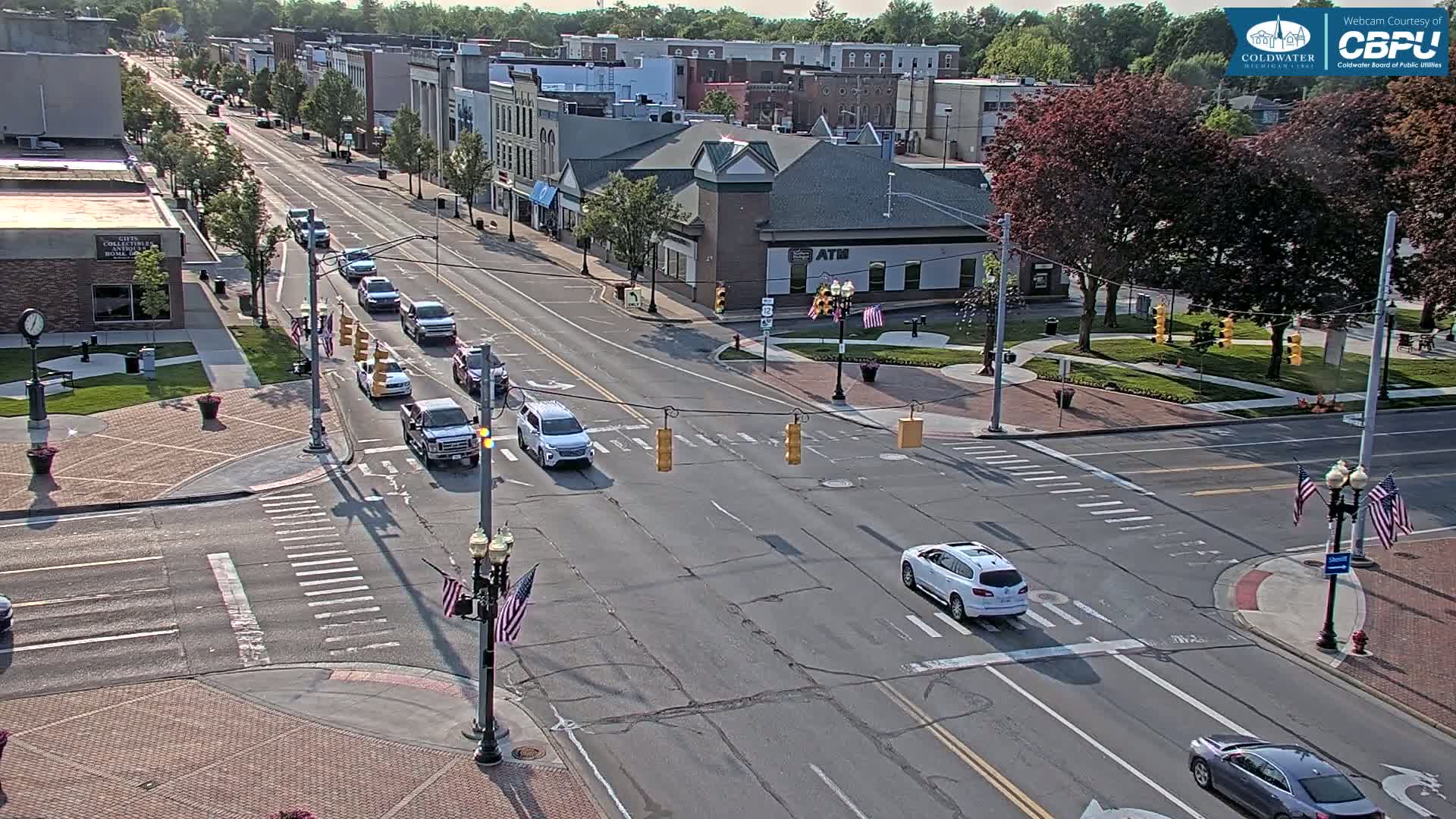 A sunny day shows a city intersection with several vehicles and a small town's buildings in the background.