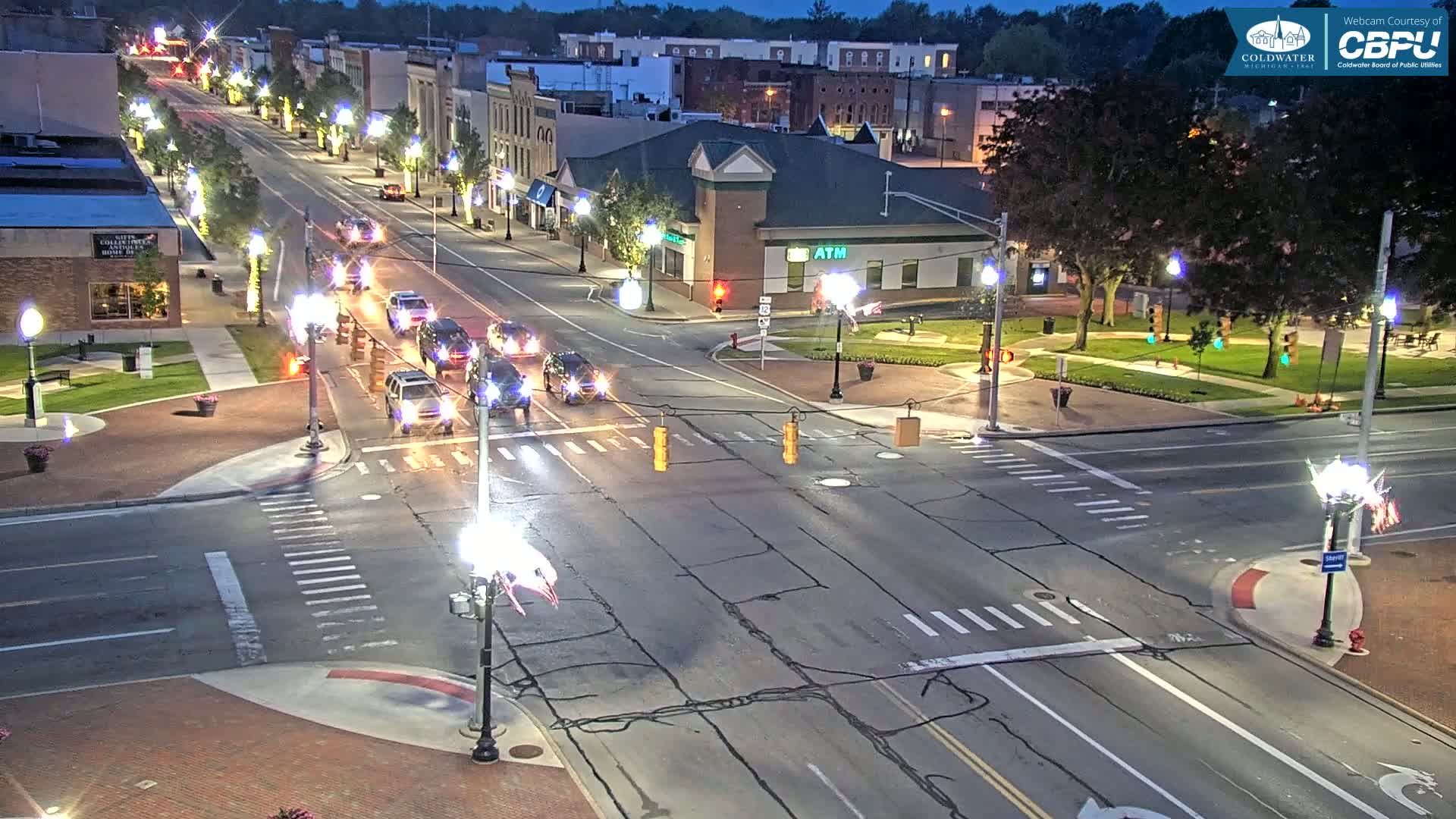 A nighttime, high-angle view of a multi-lane road intersection in a town, with several cars driving on the road and streetlights illuminating the scene.