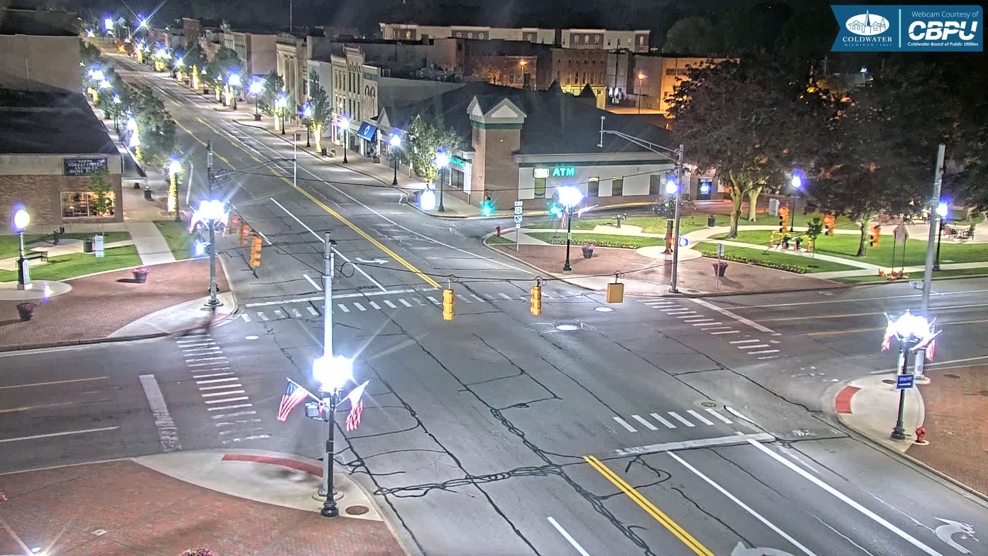 A nighttime aerial view of a city intersection with streetlights illuminating a mostly empty street and surrounding buildings.