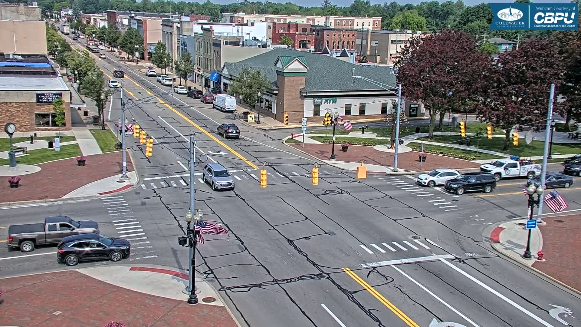 A sunny day reveals a town's street intersection with several cars, and buildings lining the streets.