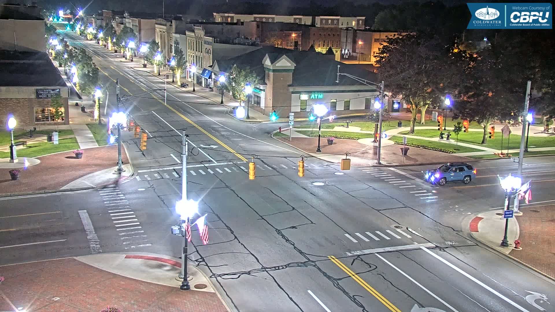 A nighttime aerial view of a city street intersection with a single vehicle at the crossing, under clear skies.